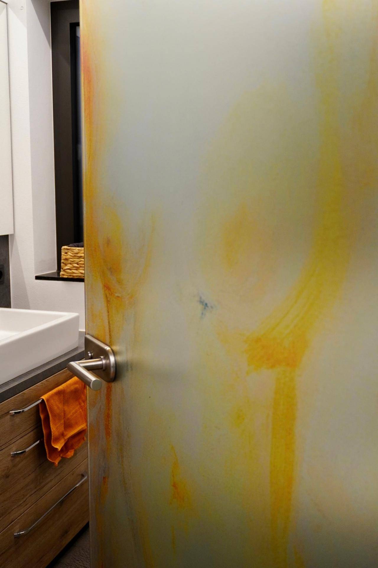 Eine leicht geöffnete Tür mit gelben Mustern, die einen Blick auf ein modernes Badezimmer freigibt.