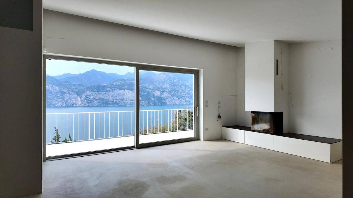 Unmöbliertes Wohnzimmer mit Betonboden, modernem Kamin und großen Schiebetüren mit Seepanorama.