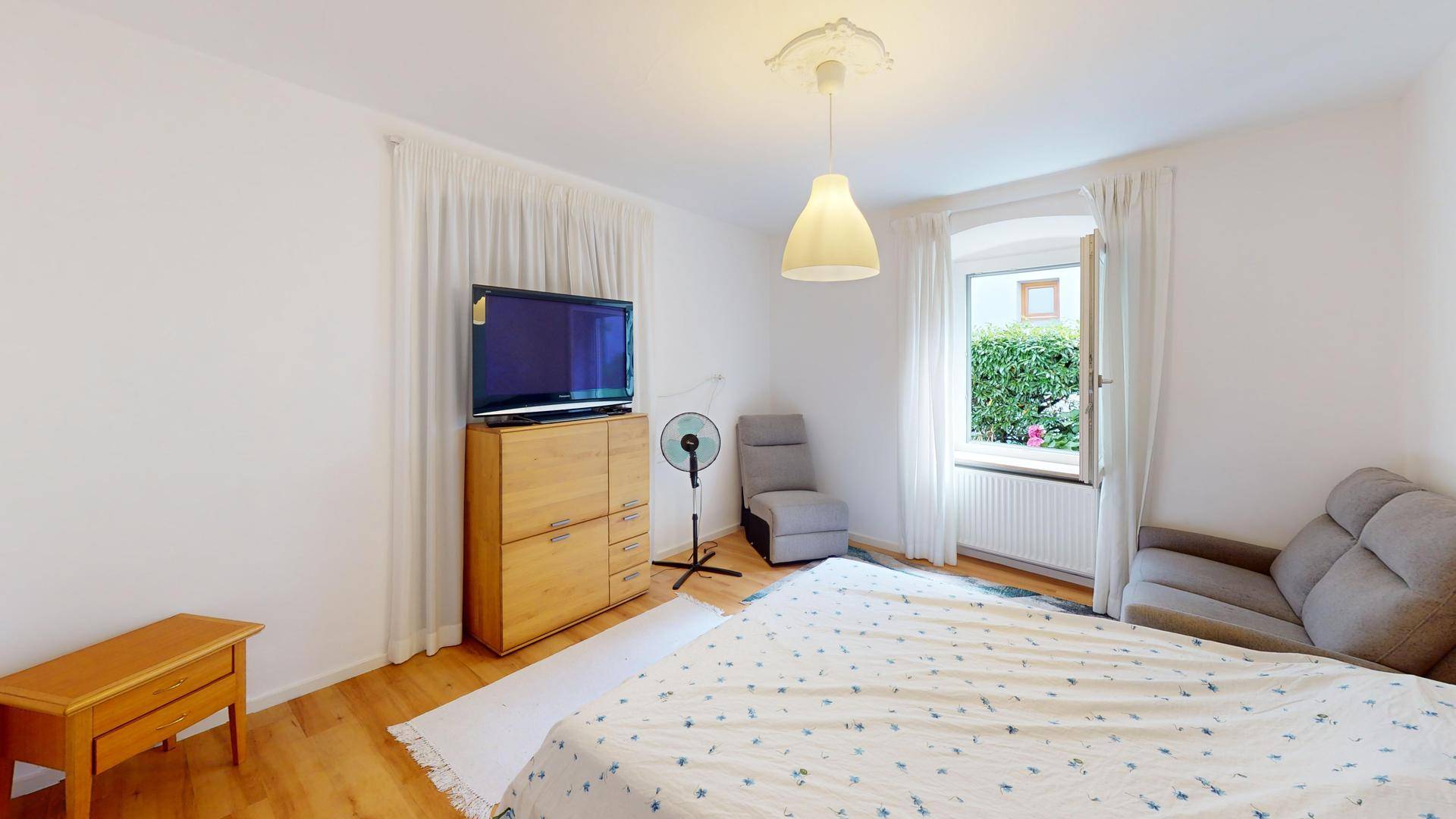 Schlafzimmer mit Doppelbett, Fernseher und einem Fenster, das einen Blick in den Garten bietet.