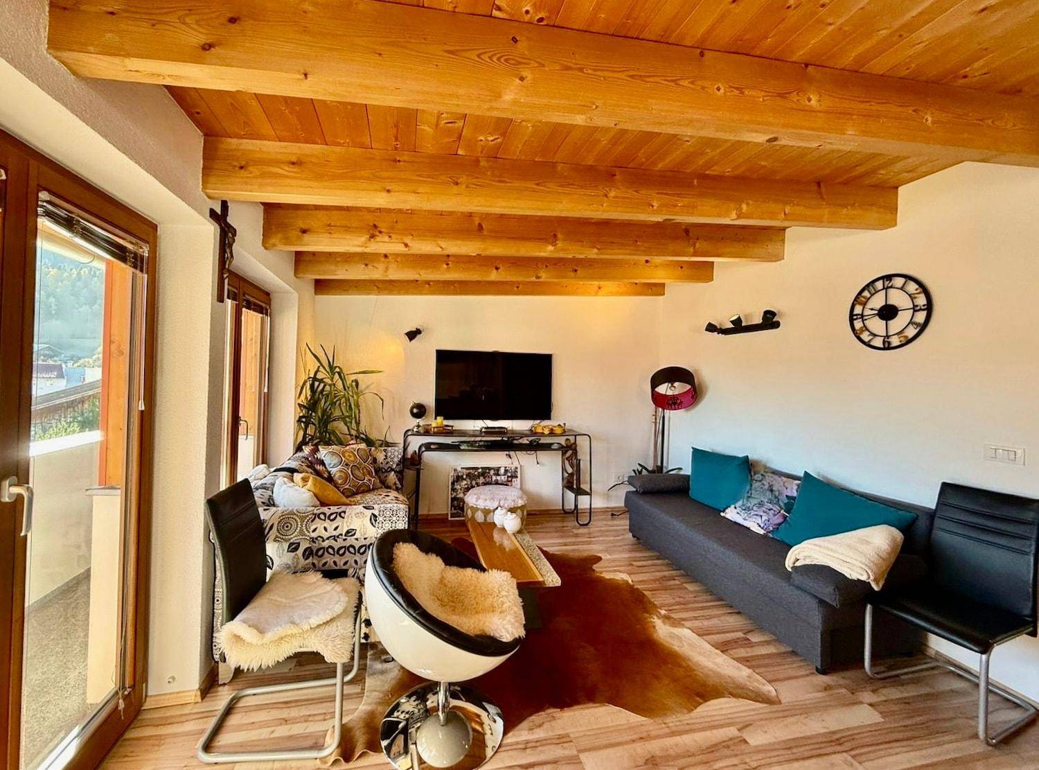 Gemütliches Wohnzimmer mit Holzbalkendecke, Parkettboden und Zugang zu einem Außenbereich.