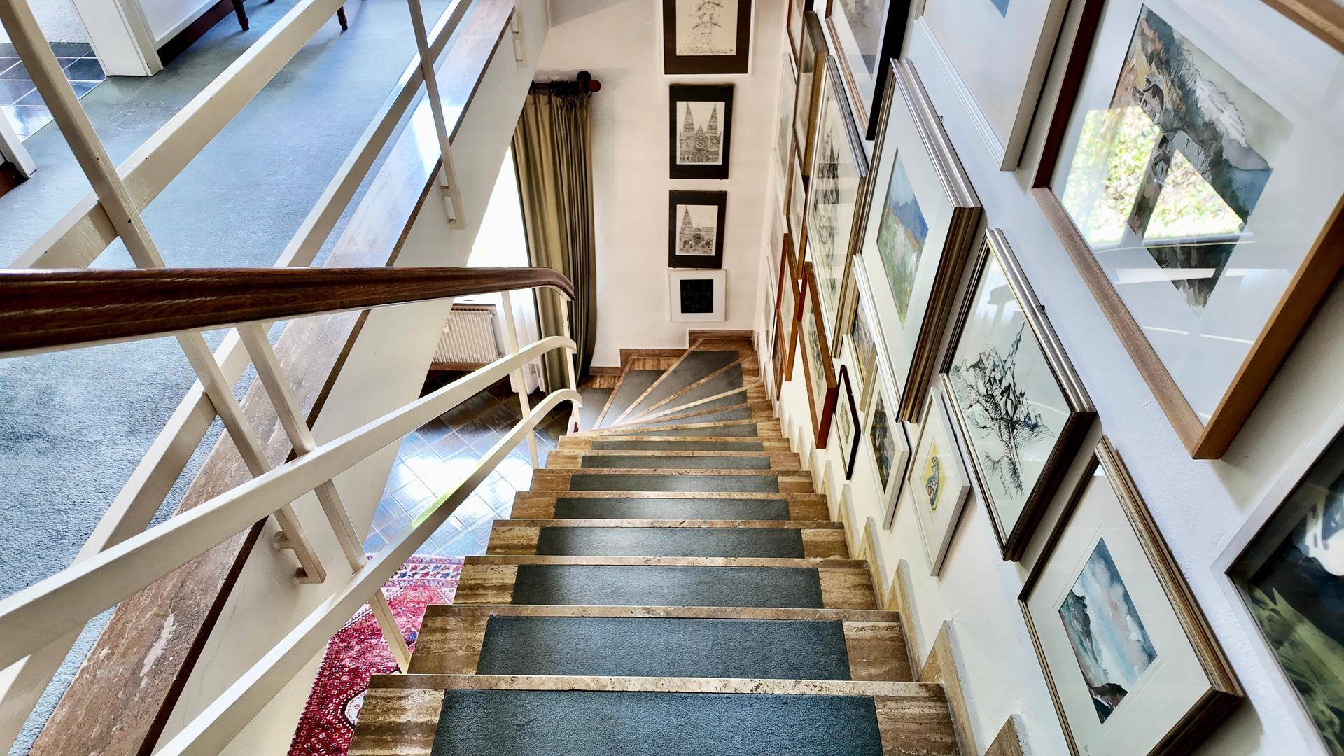 Elegante Treppe mit Holzgeländer und einer Galerie von gerahmten Bildern entlang der Wand, von oben gesehen.