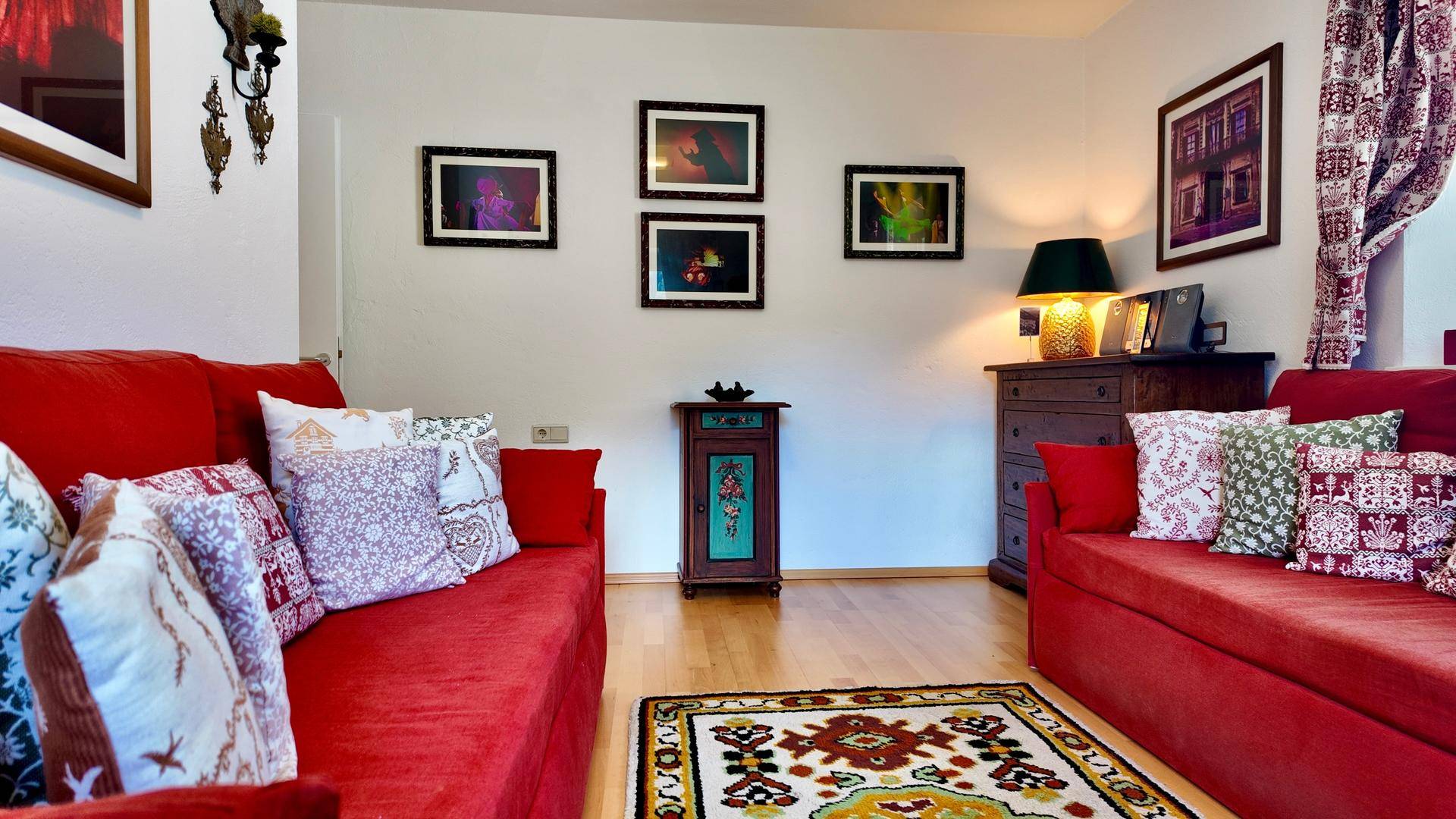 Geräumiges Wohnzimmer mit zwei roten Sofas, einem gemusterten Teppich und traditioneller Dekoration.