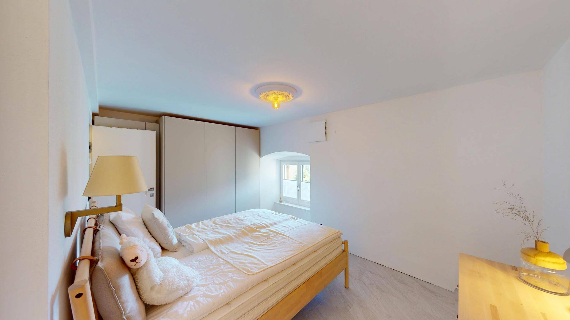 Helles Schlafzimmer mit schlichtem Design, Holzbett und einem Fenster für Tageslicht.
