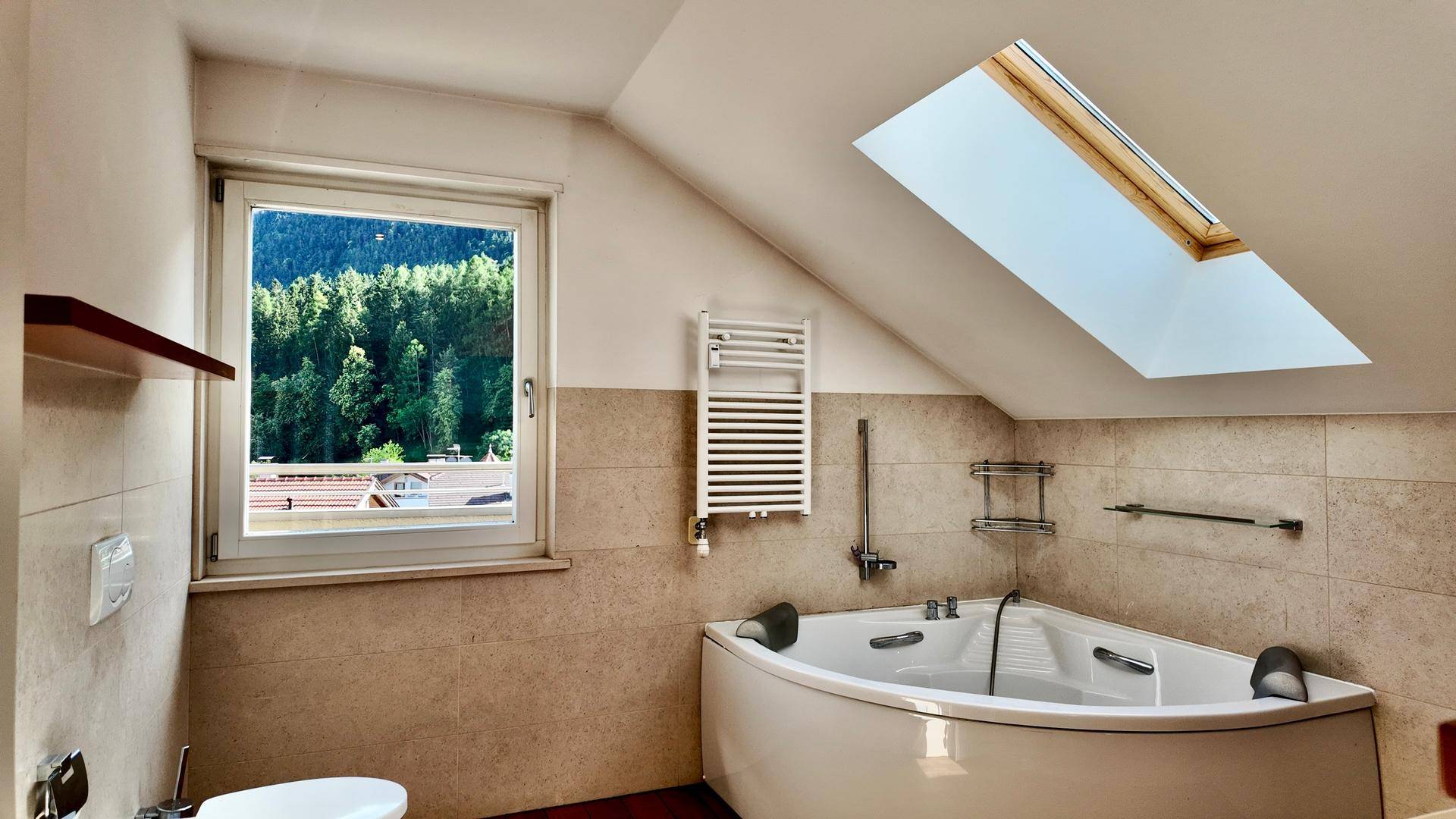 Badezimmer im Dachgeschoss mit Eckbadewanne, Dachfenster und Blick ins Grüne.