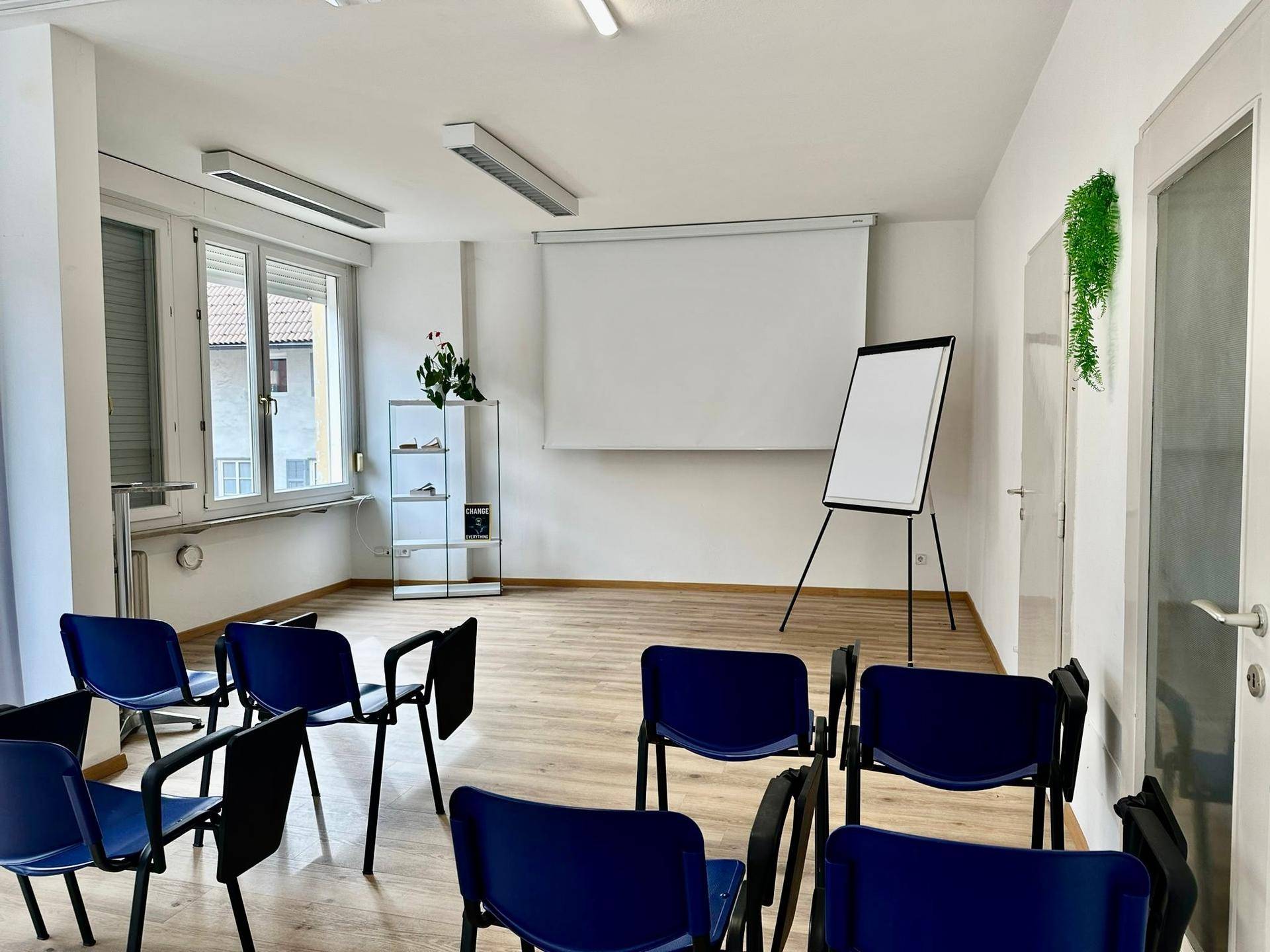 Moderner Schulungsraum mit Projektionsfläche, Flipchart und bequemen Stühlen für Teilnehmer.