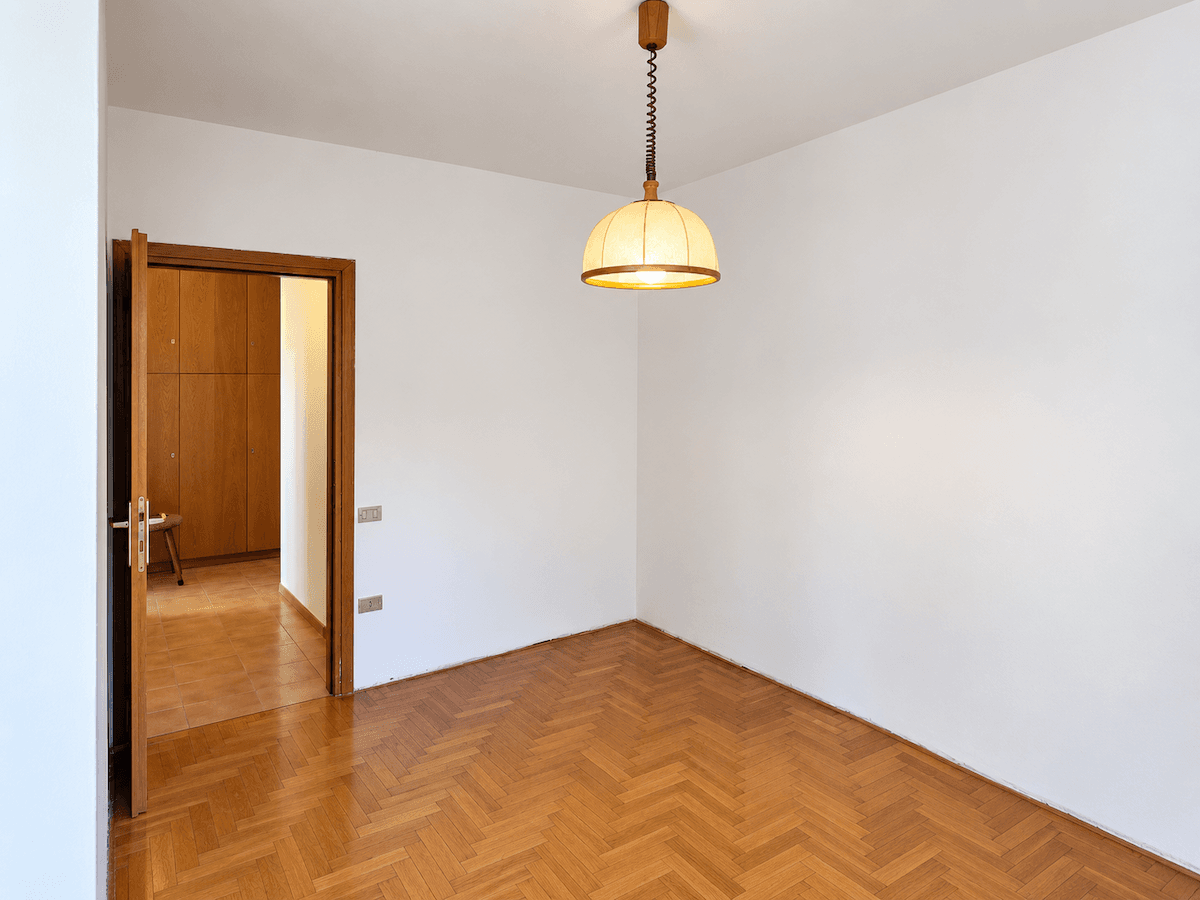 Leeres Zimmer mit Fischgrätparkett und Zugang zu einem weiteren Raum mit Holzschränken.