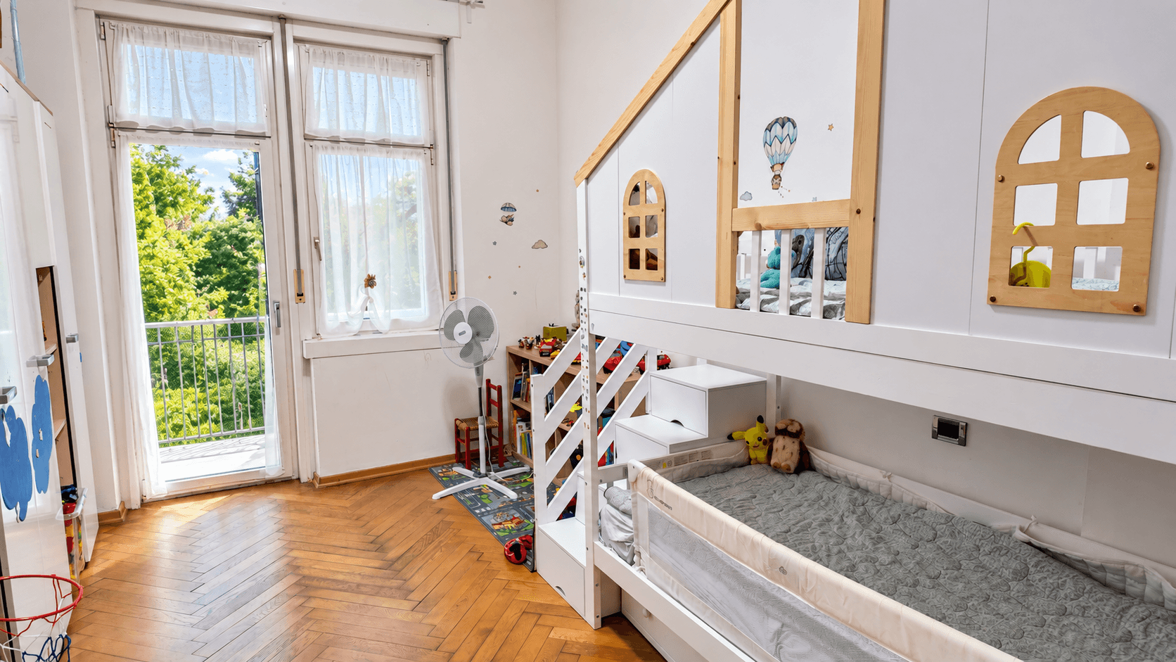 Kinderzimmer mit Etagenbett in Hausform, Holzboden und Zugang zum Balkon.