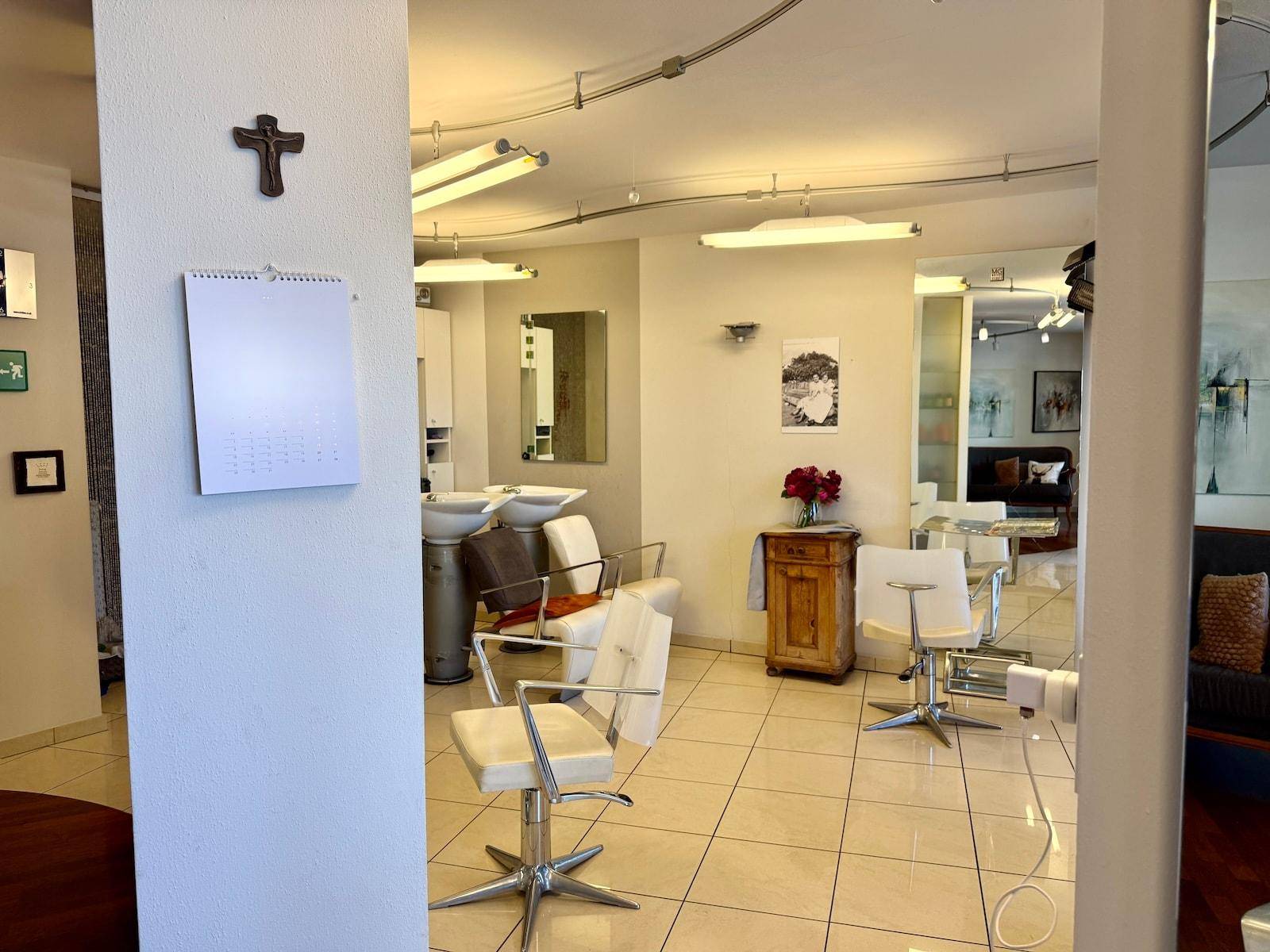 Friseursalon mit mehreren Bedienplätzen, Waschbecken und einem Kalender an der Wand.