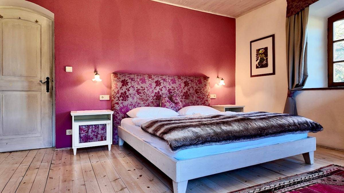 Helles Schlafzimmer mit rosa Akzentwand, Holzboden und einem bequemen Bett mit gemustertem Kopfteil.