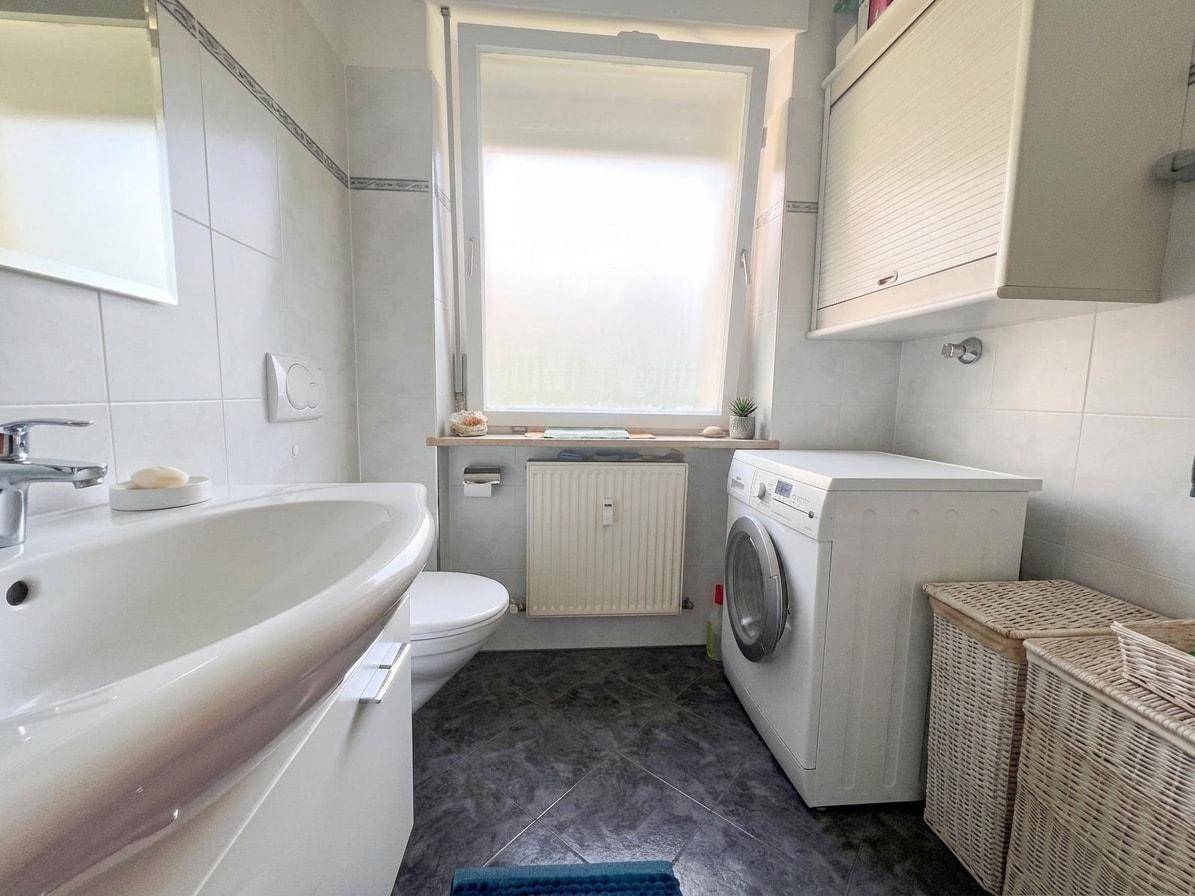 Helles Badezimmer mit Fenster, Waschmaschine, WC und Waschbecken.