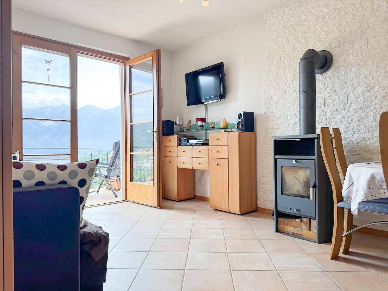 Wohnzimmer mit Kaminofen, Fliesenboden und Balkonzugang, bietet einen weiten Blick auf die Berge.