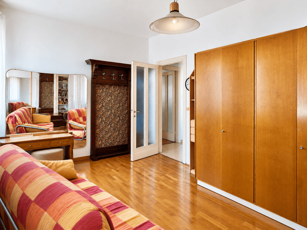 Schlafzimmer mit Holzschrank, Schlafsofa und einem großen Spiegel, der den Raum optisch erweitert.