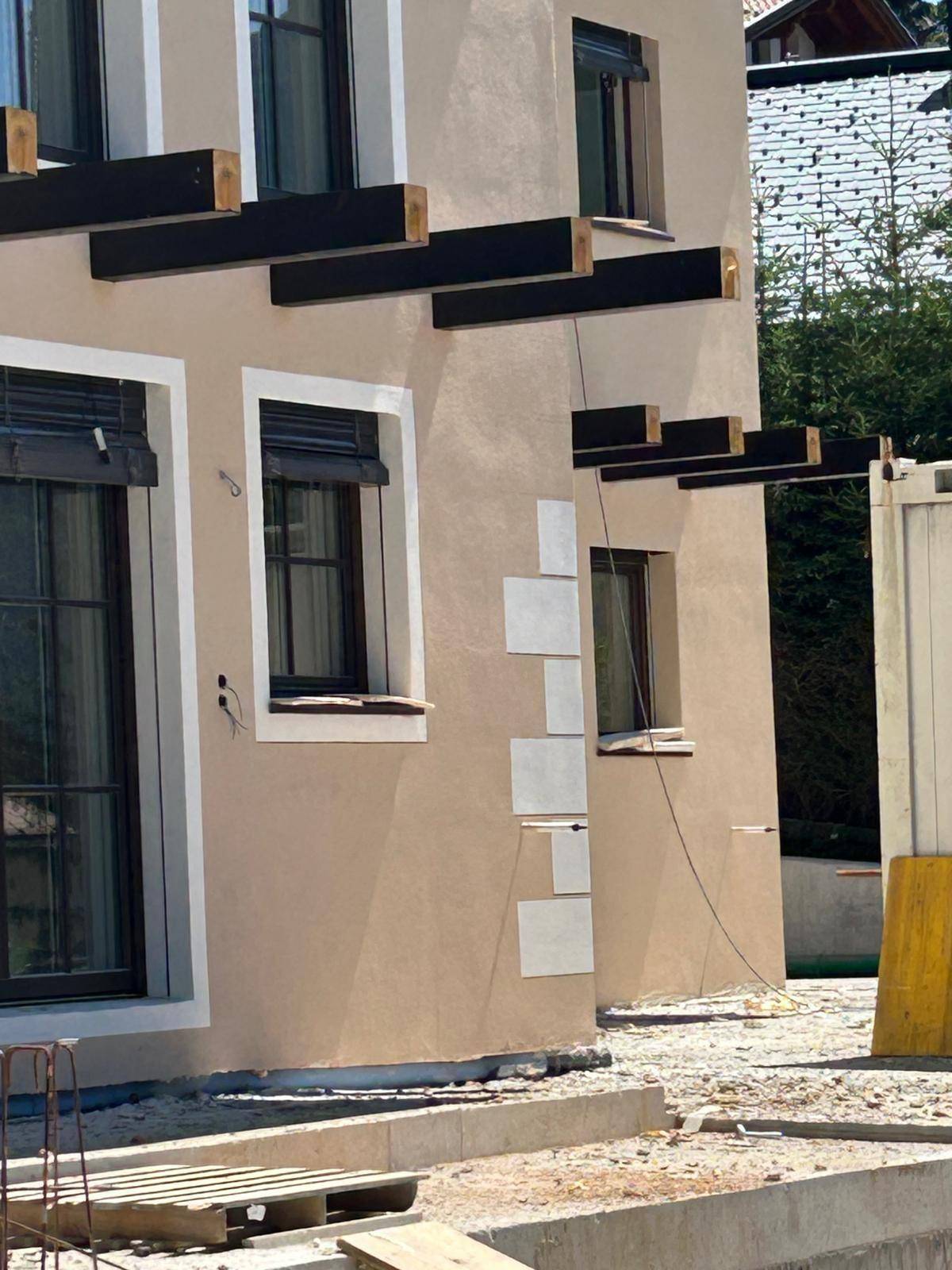 Nahaufnahme der beigen Fassade des Neubaus mit schwarzen Fenstern und vorbereiteten Balkonstützen.