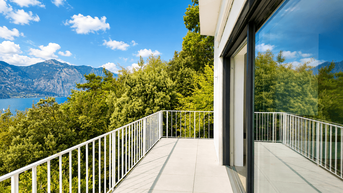 Heller Balkon mit weißen Geländern und großen Glasschiebetüren, bietet einen weiten Blick auf den See.