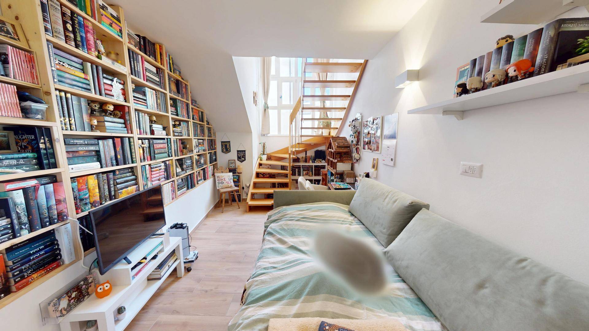 Heller Wohnbereich mit Sofa, Bücherregal und Blick auf die Holztreppe.