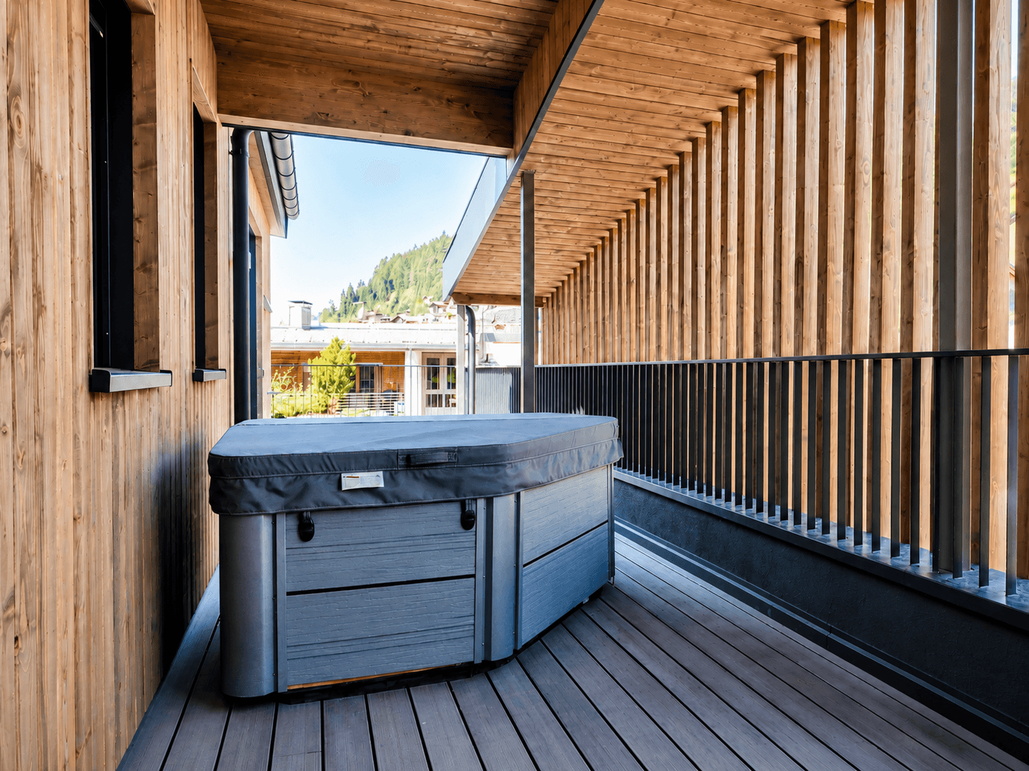 Überdachte Terrasse mit einem modernen Whirlpool, umgeben von Holzverkleidung und Lattenelementen.