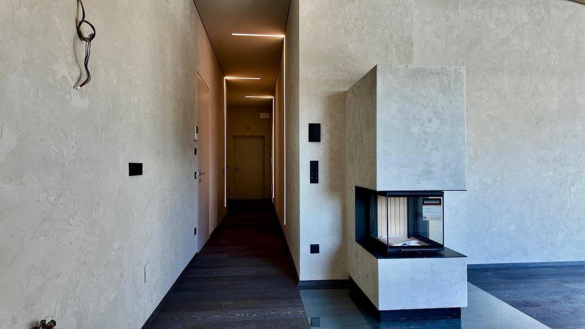 Moderner Flur mit strukturierten Wänden, dunklem Holzboden und integrierter Beleuchtung neben einem Kamin.