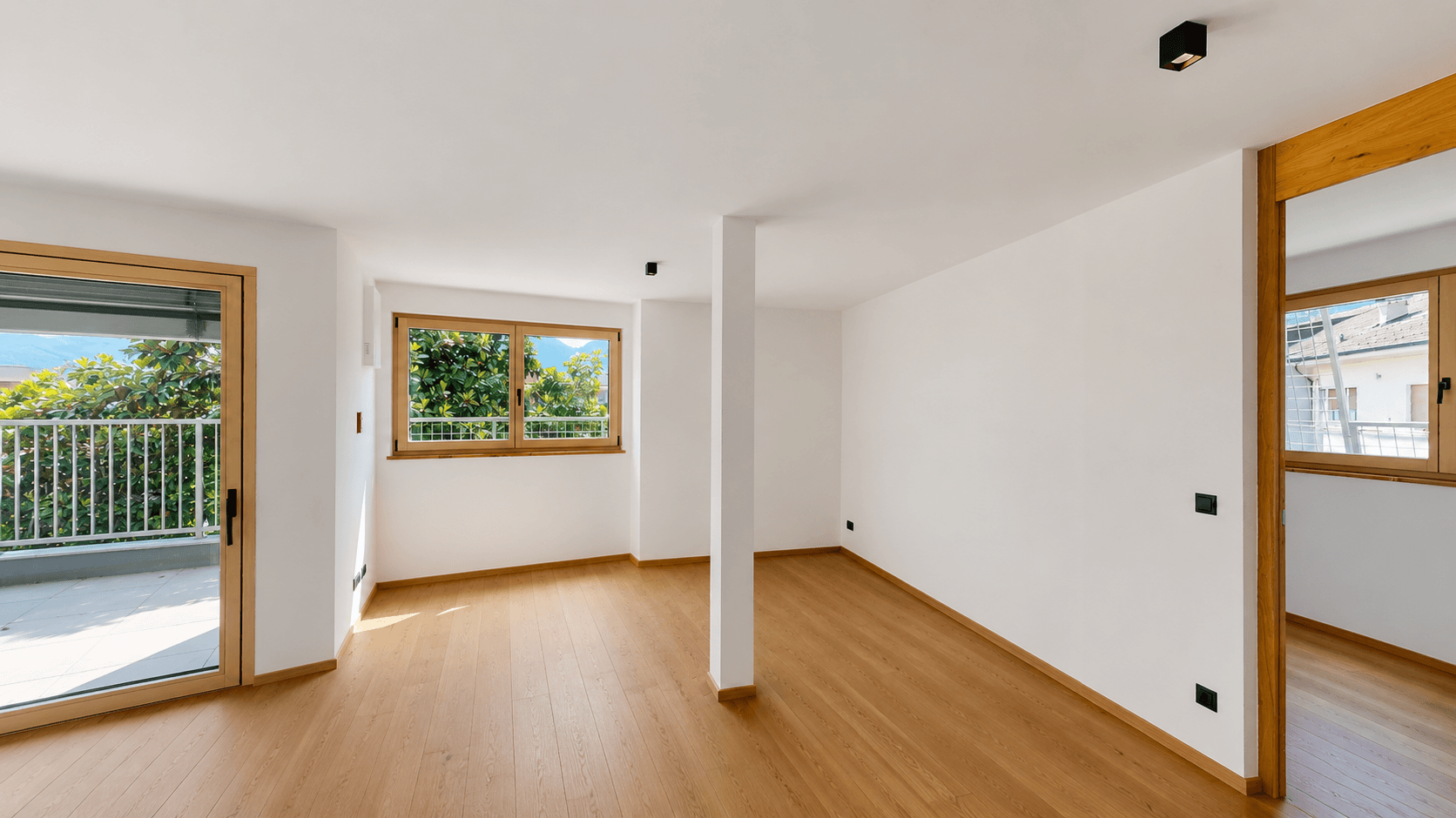 Heller Wohnbereich mit Holzboden, weißen Wänden und Zugang zu einem Außenbereich.