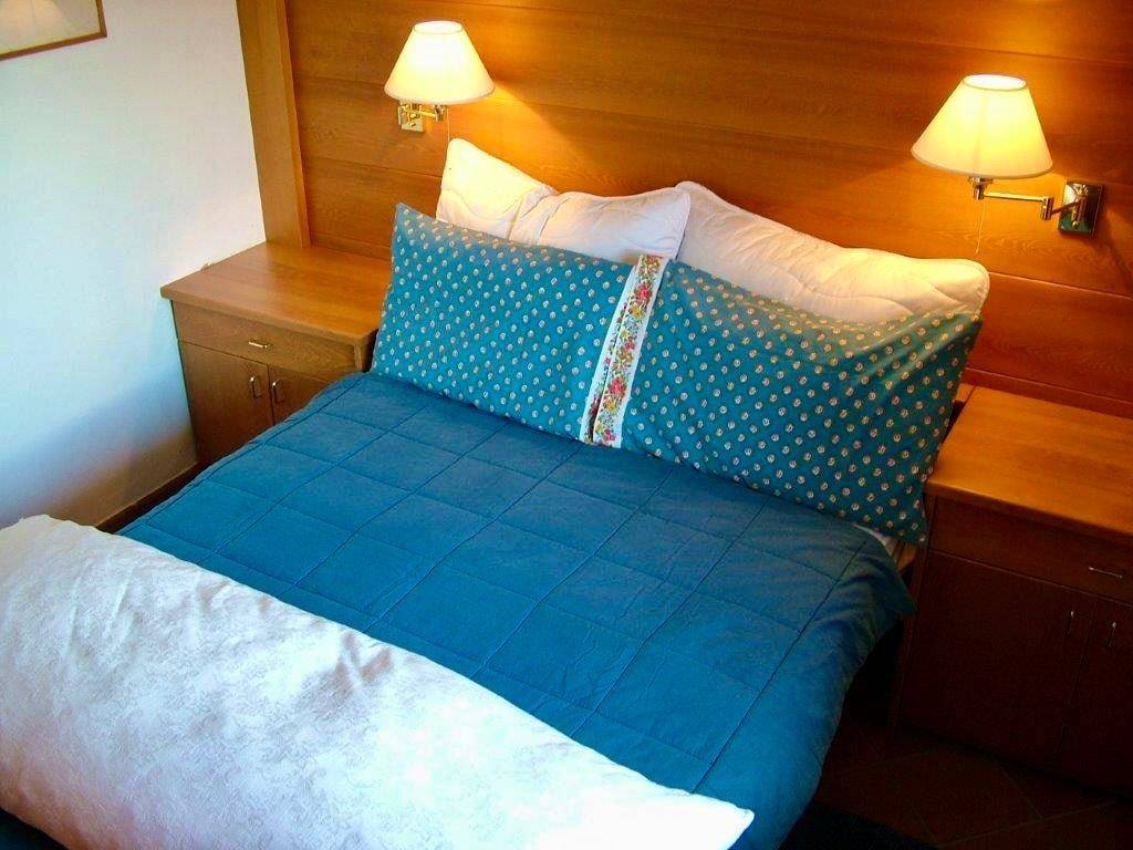 Schlafzimmer mit Doppelbett, Holzkopfteil und Nachttischen, beleuchtet von Wandlampen.