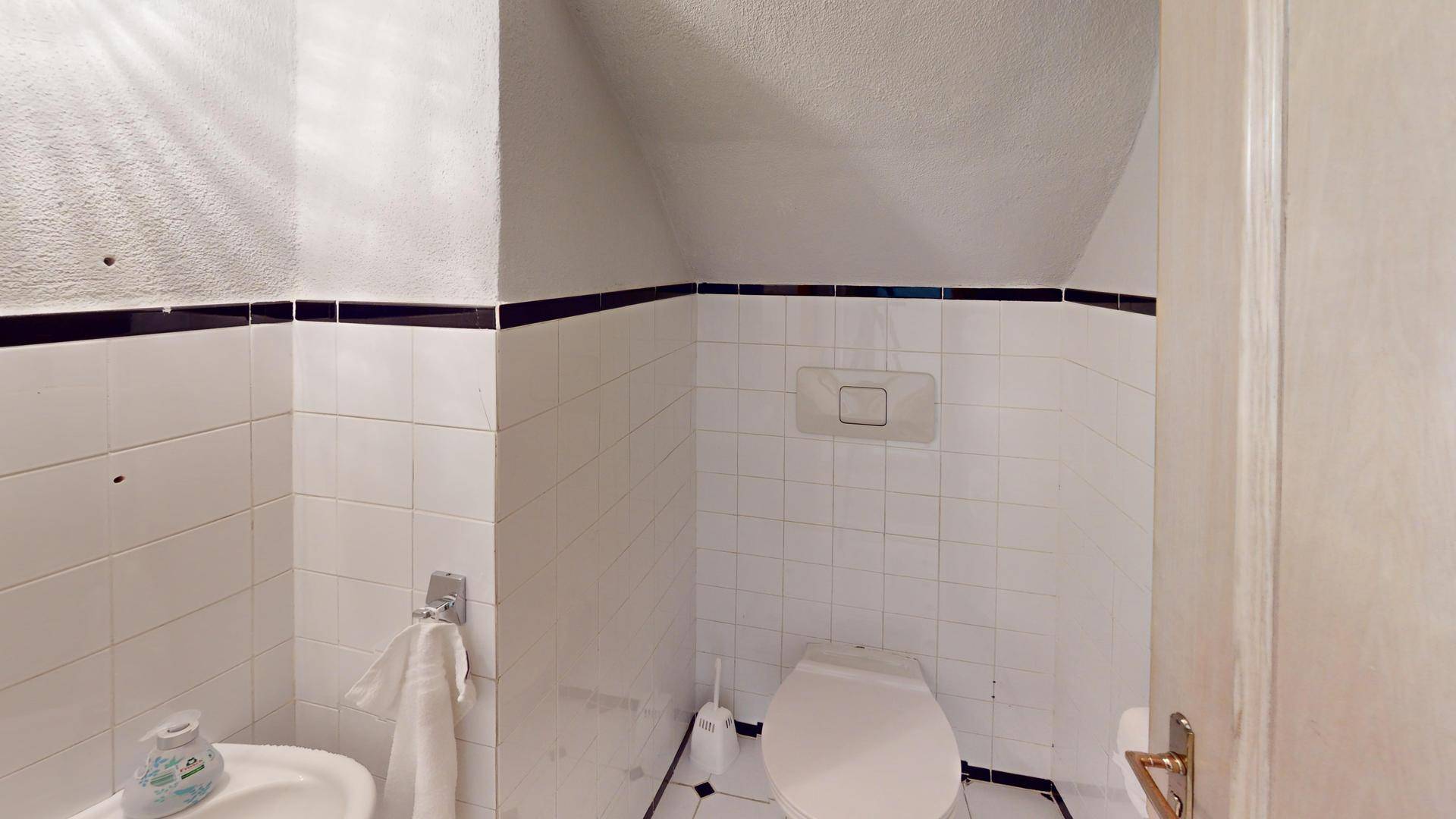 Einfaches Gäste-WC mit weißen Fliesen und schwarzem Dekorstreifen.