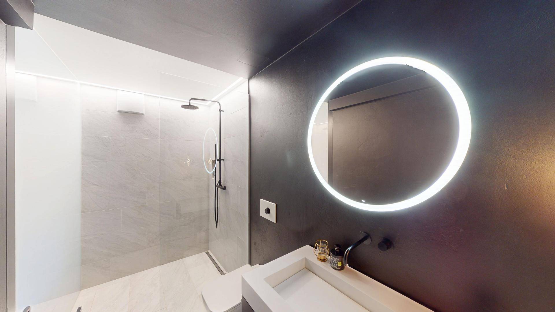 Detailansicht des modernen Badezimmers mit Waschtisch, beleuchtetem Spiegel und Regendusche.
