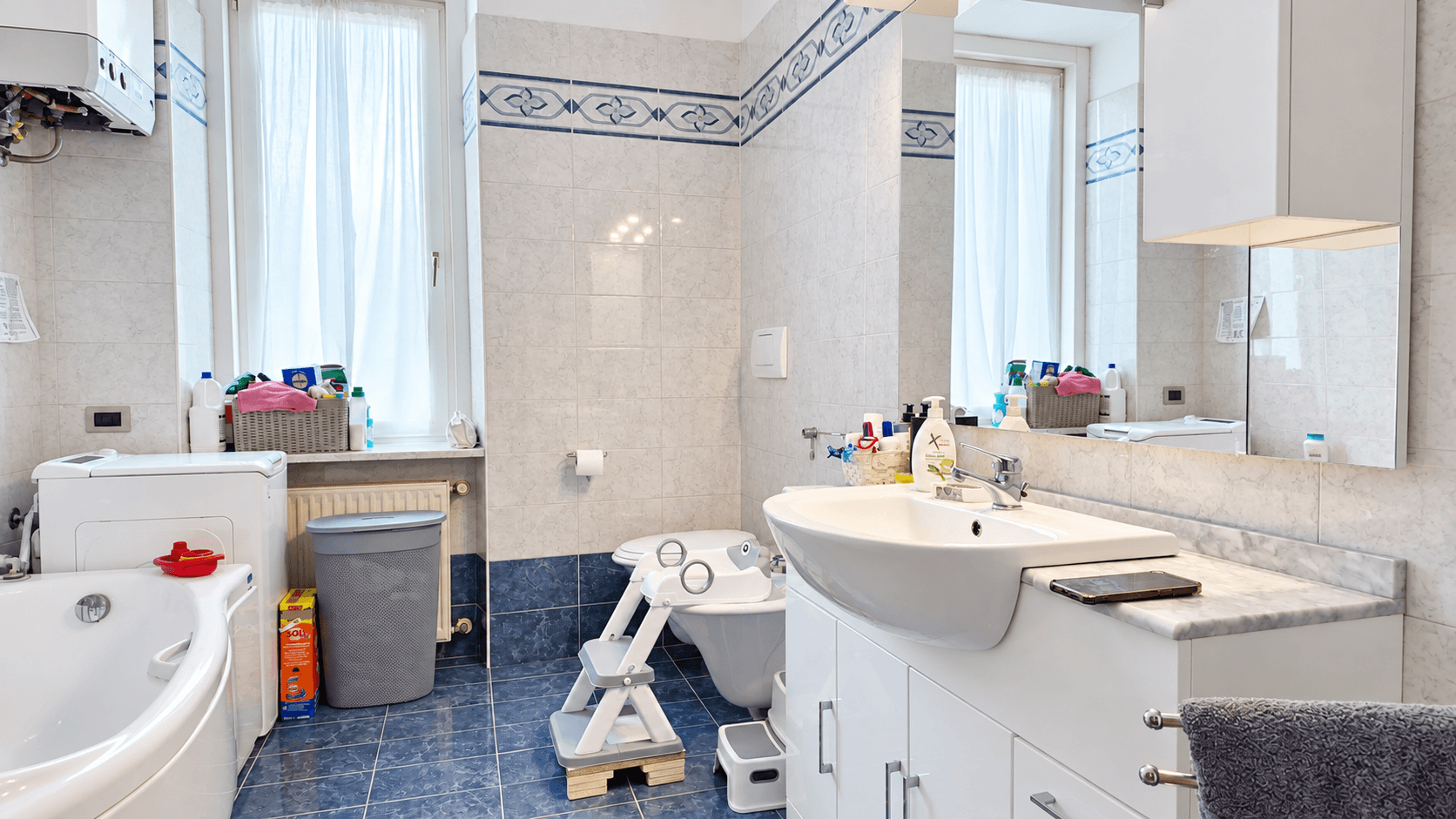 Badezimmer mit blauen Fliesen, Badewanne, Waschbecken und Fenster.