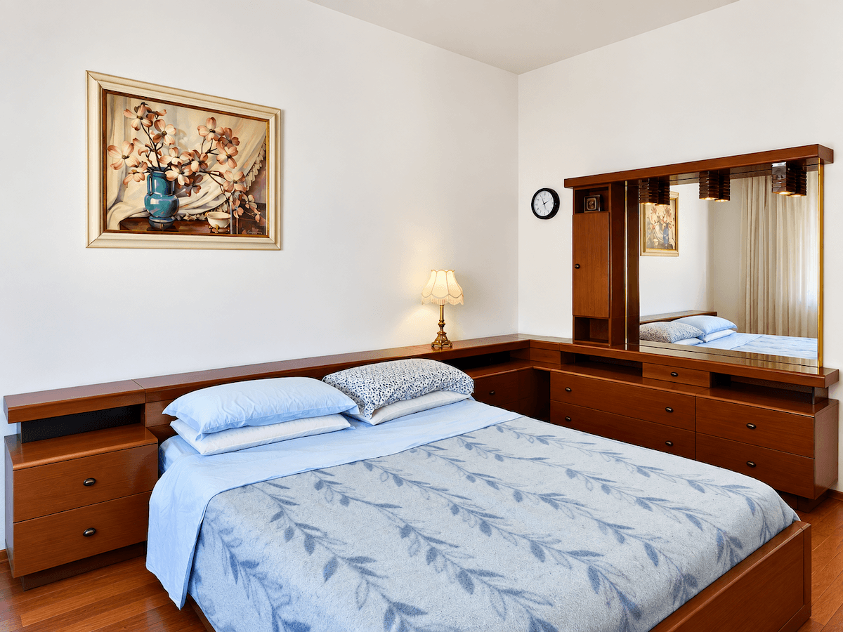 Schlafzimmer mit Doppelbett, passenden Holzmöbeln und einem großen Spiegel über der Kommode.