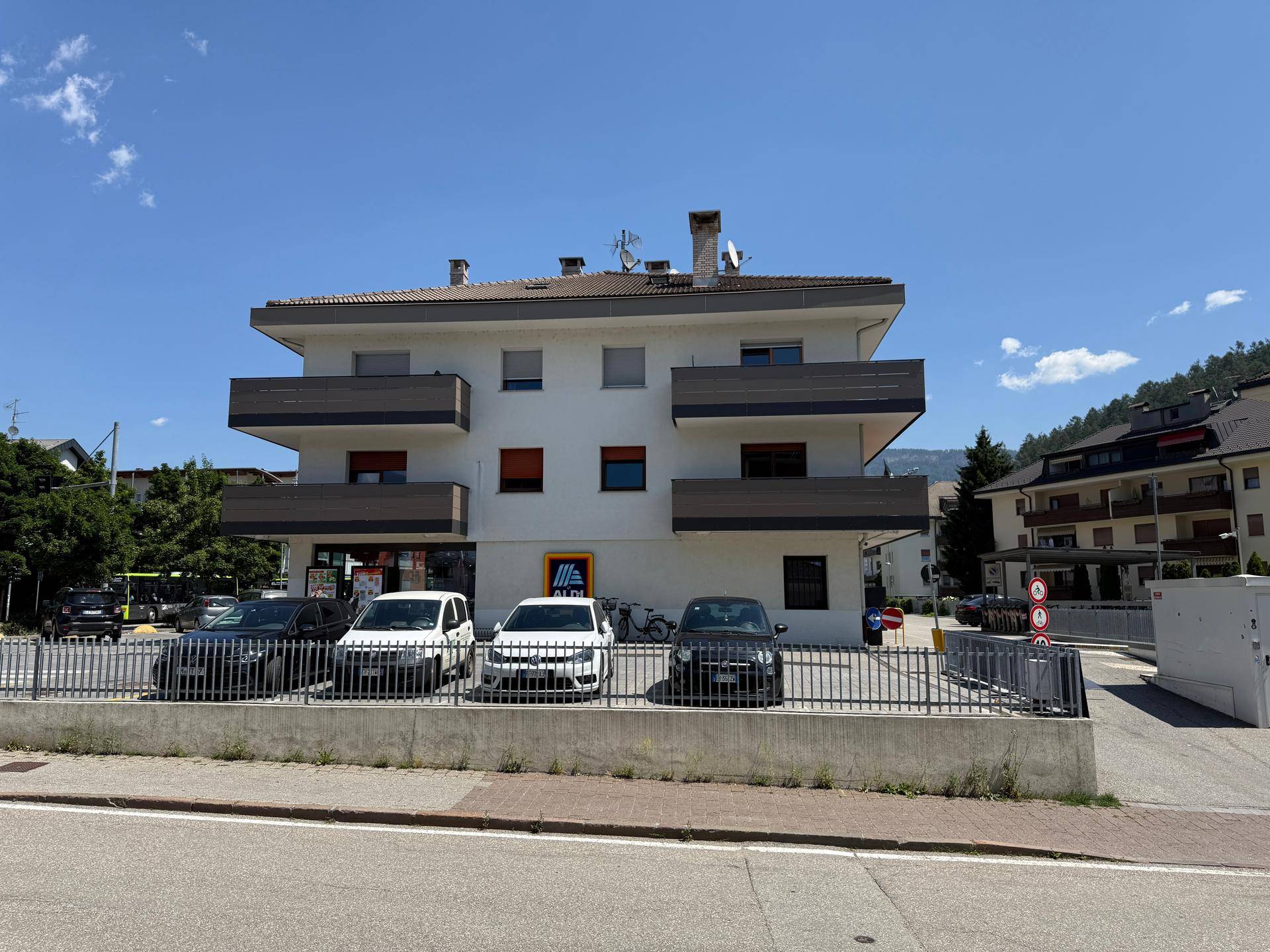 Mehrfamilienhaus mit Balkonen und einem Supermarkt im Erdgeschoss an einem sonnigen Tag.
