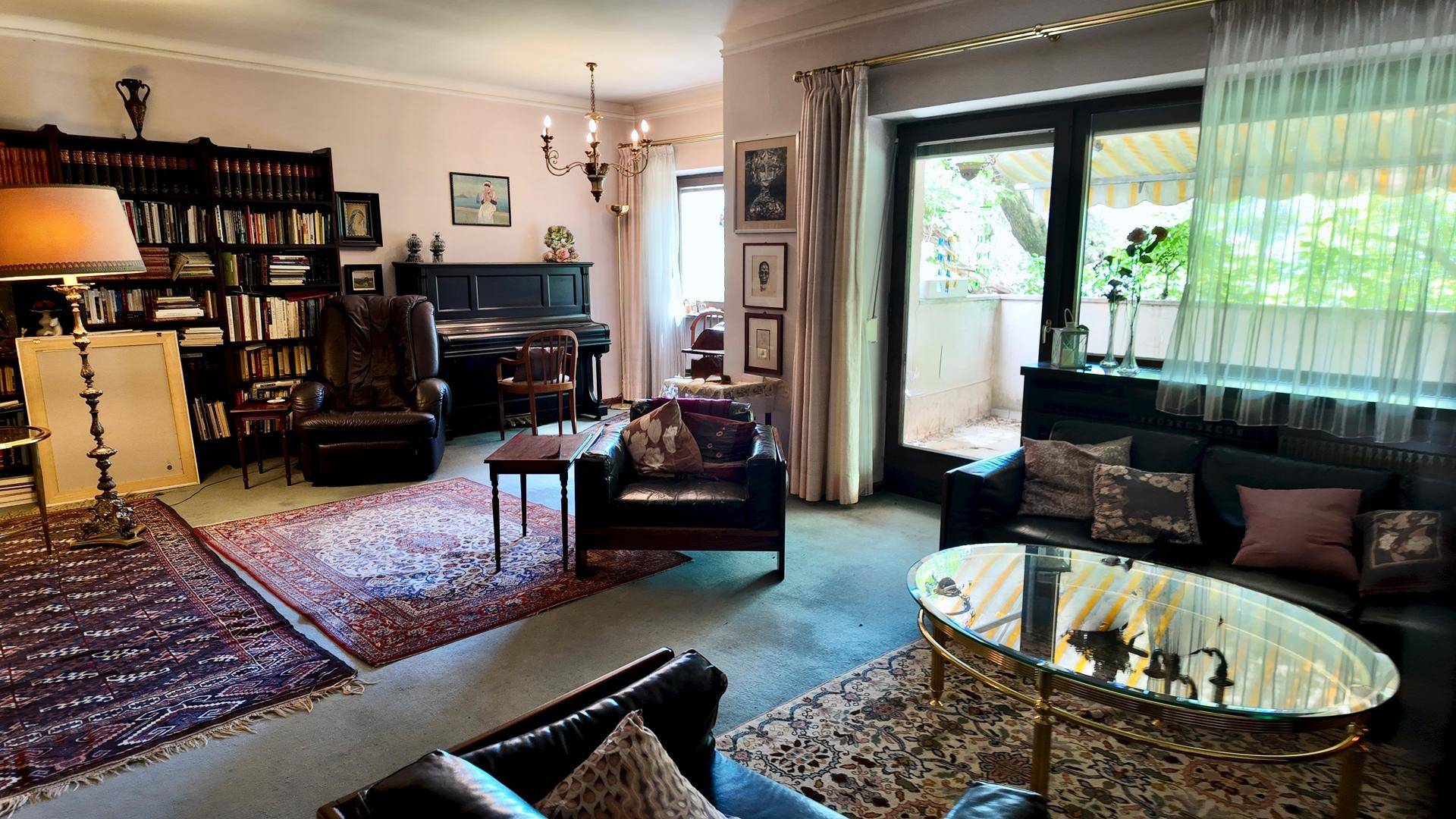 Geräumiges Wohnzimmer mit Teppichboden, Ledersofas, Klavier und Balkonzugang.