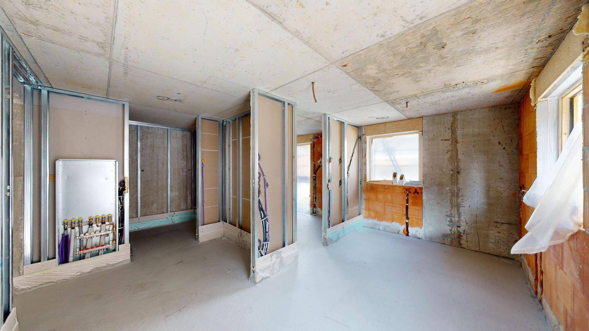 Innenraum im Rohbau mit Trockenbauwänden, sichtbaren Installationen und Fenstern.