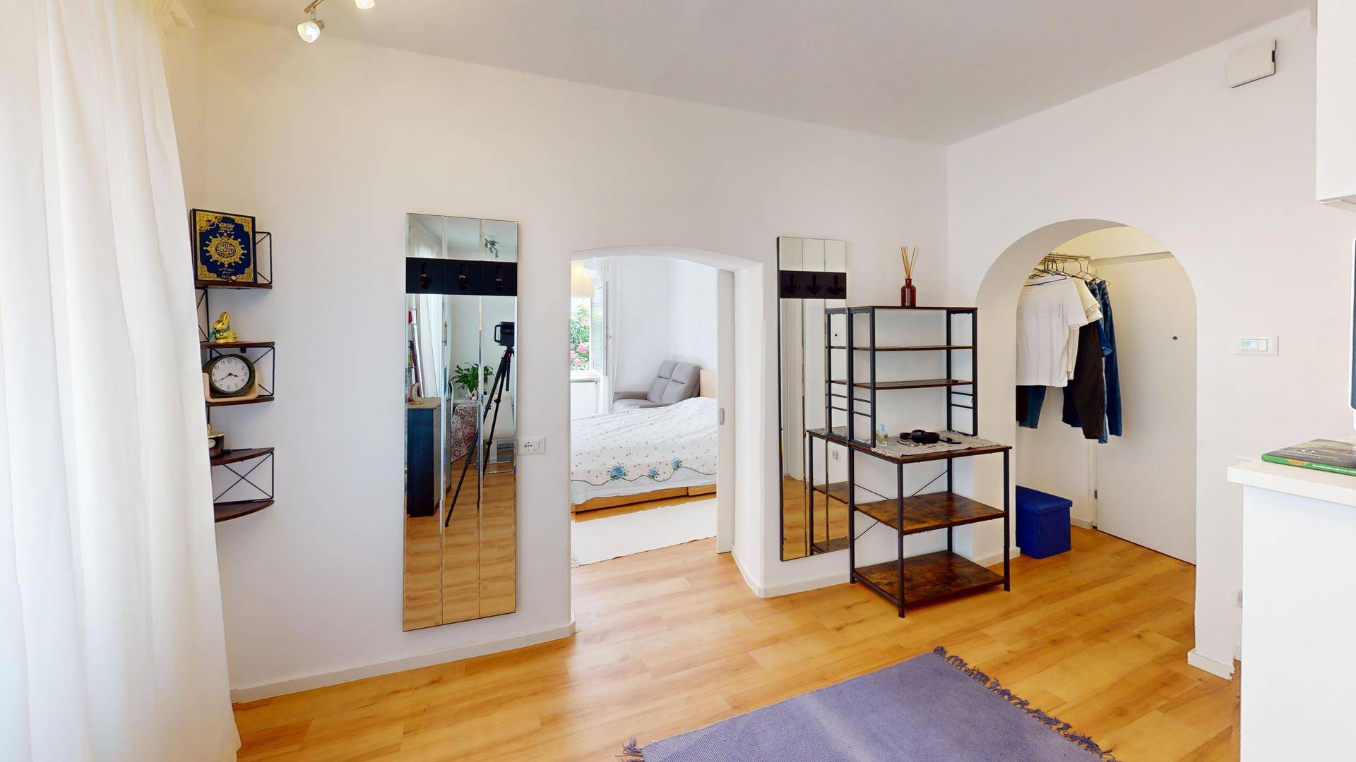 Offener Wohnbereich mit Holzboden, Spiegeln und Blick in das angrenzende Schlafzimmer.