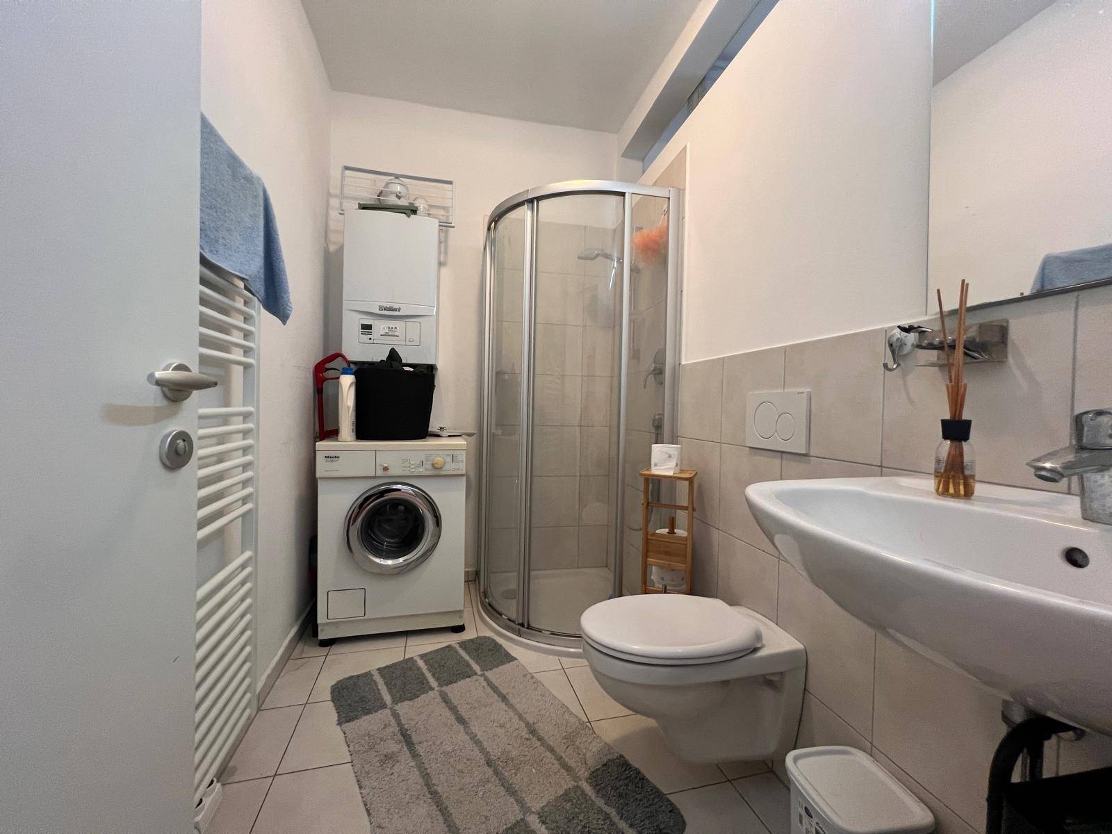 Funktionales Badezimmer mit Duschkabine, WC, Waschbecken und Waschmaschine.