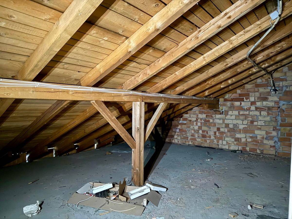 Unausgebauter Dachboden mit sichtbaren Holzbalken und Ziegelwänden, bietet Potenzial für Ausbau.