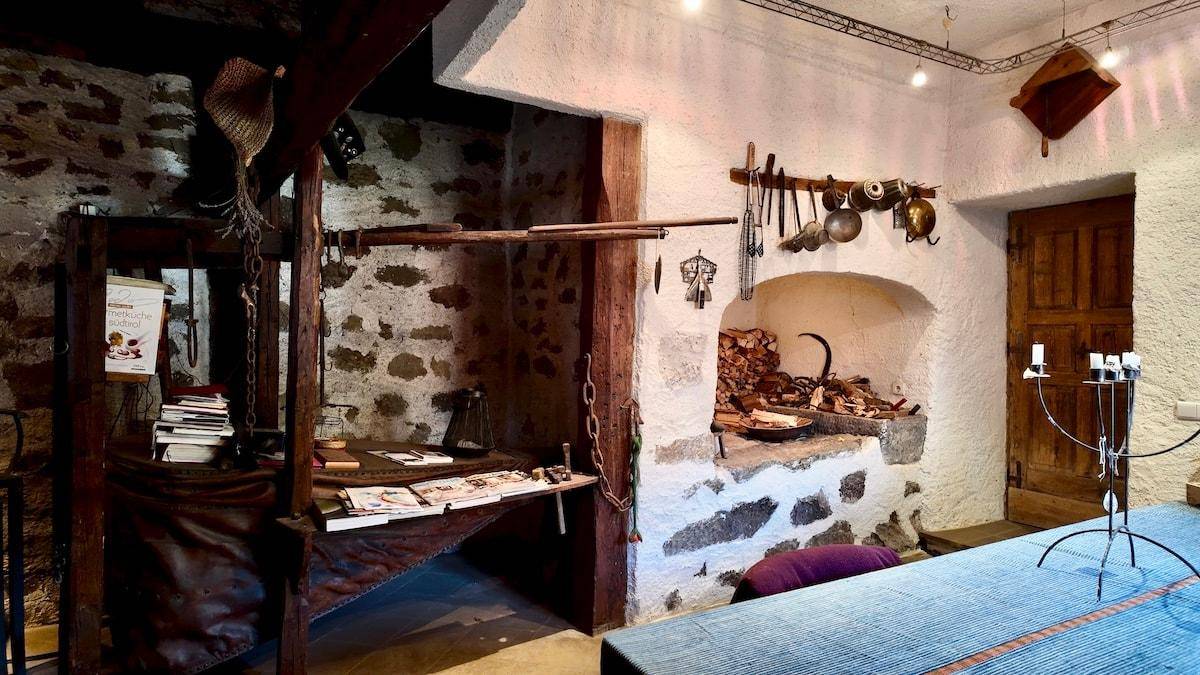 Rustikale Küche mit Steinwänden, traditionellem Ofen und antiken Küchenutensilien, die eine historische Atmosphäre schafft.