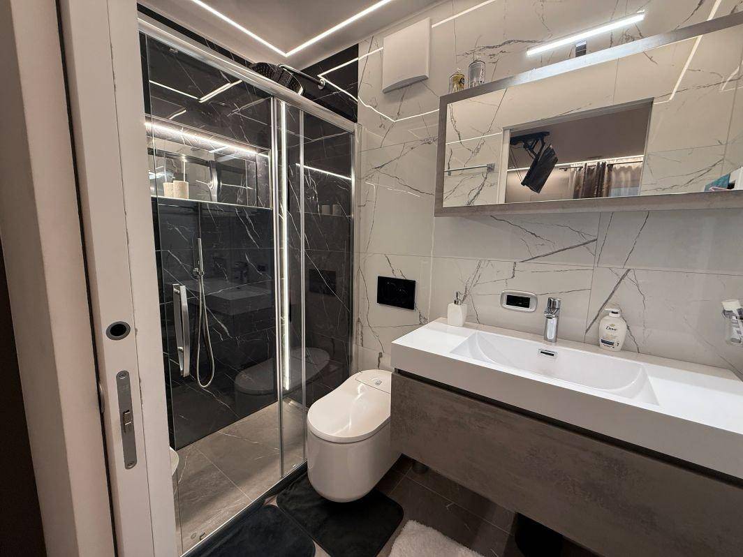Elegantes Badezimmer mit Marmorfliesen, begehbarer Dusche und modernem Doppelwaschbecken.