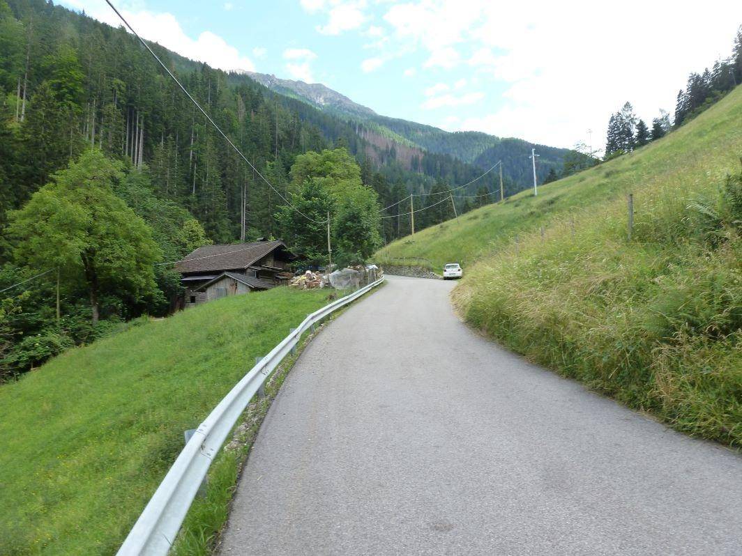 Serpentinenstraße führt durch eine grüne Berglandschaft zum abgelegenen Holzhaus, umgeben von dichtem Wald.