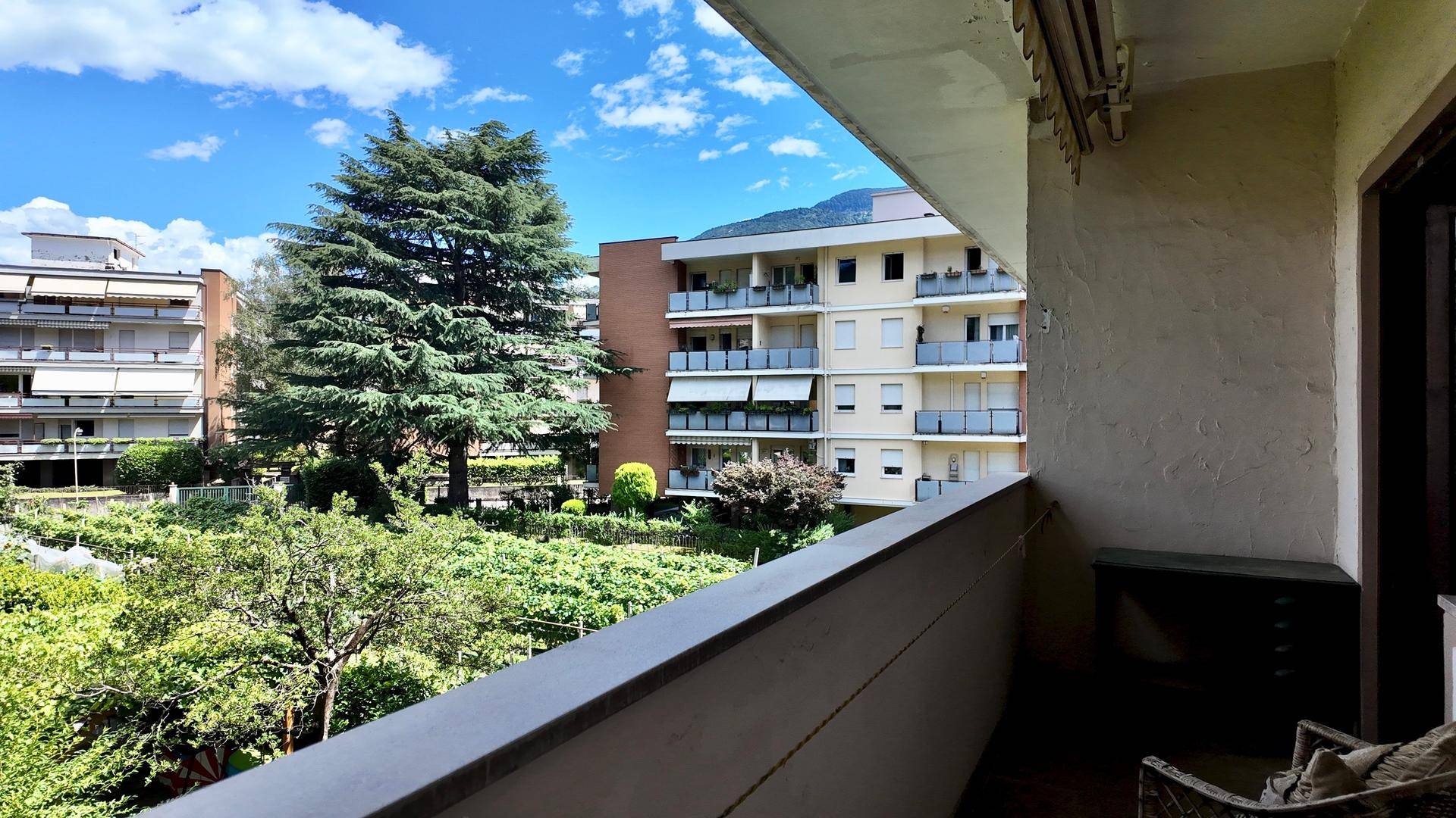Balkon mit weitem Blick auf eine grüne Gartenanlage und umliegende Wohngebäude unter blauem Himmel.