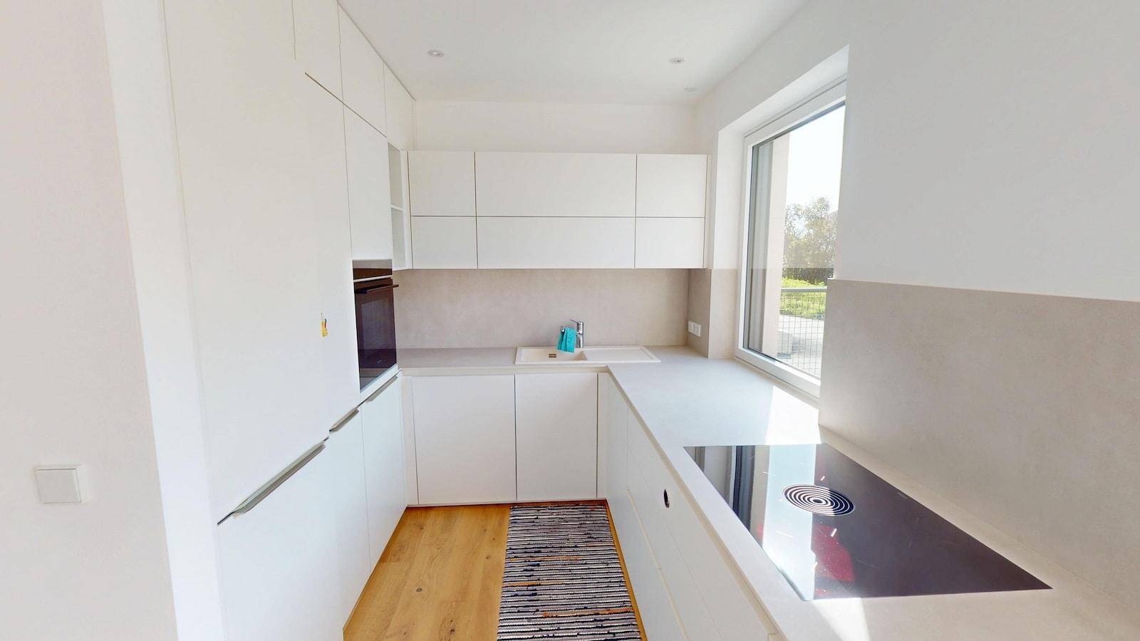 Moderne, helle Küche mit weißen Schränken, integrierten Geräten und Induktionskochfeld.