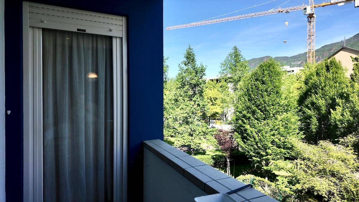 Balkon mit Blick auf Bäume und eine Baustelle mit Kran im Hintergrund.