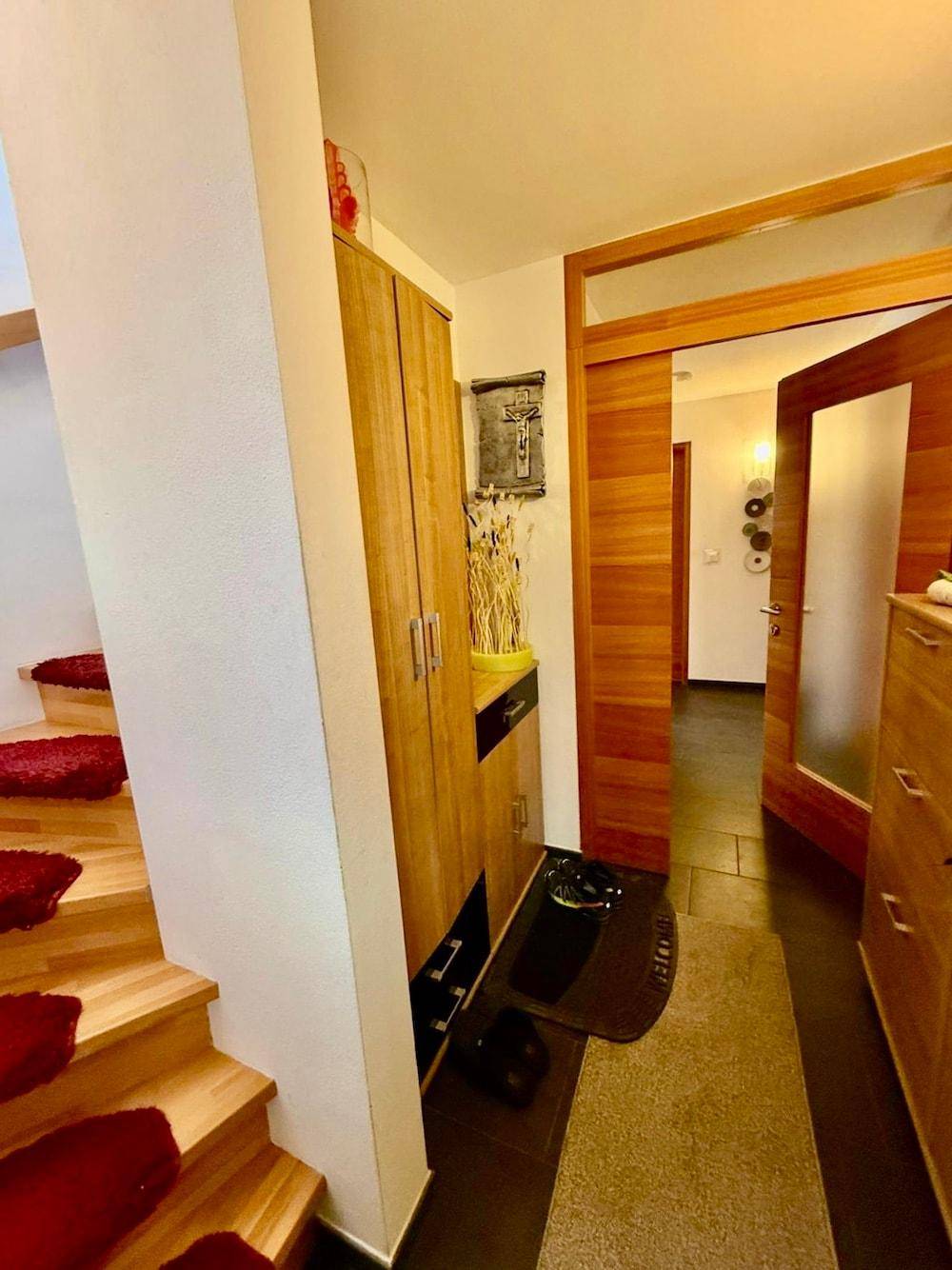 Eingangsbereich mit Holztreppe, Garderobenschrank und dunklem Fliesenboden.