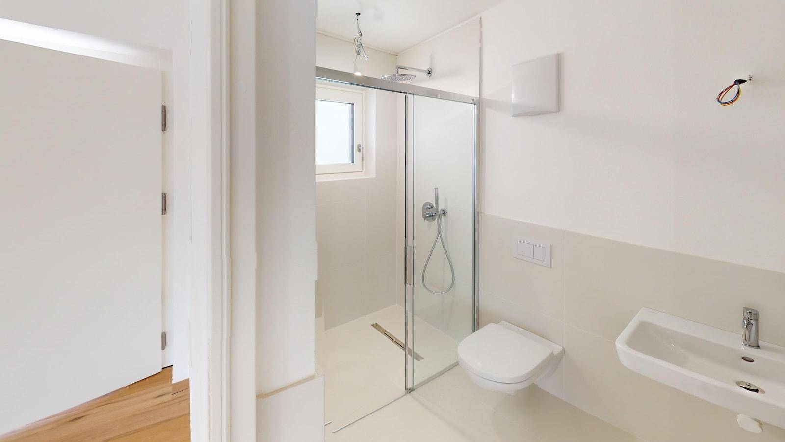 Helles Badezimmer mit ebenerdiger Dusche, WC und Fenster, modern gefliest und in neuwertigem Zustand.
