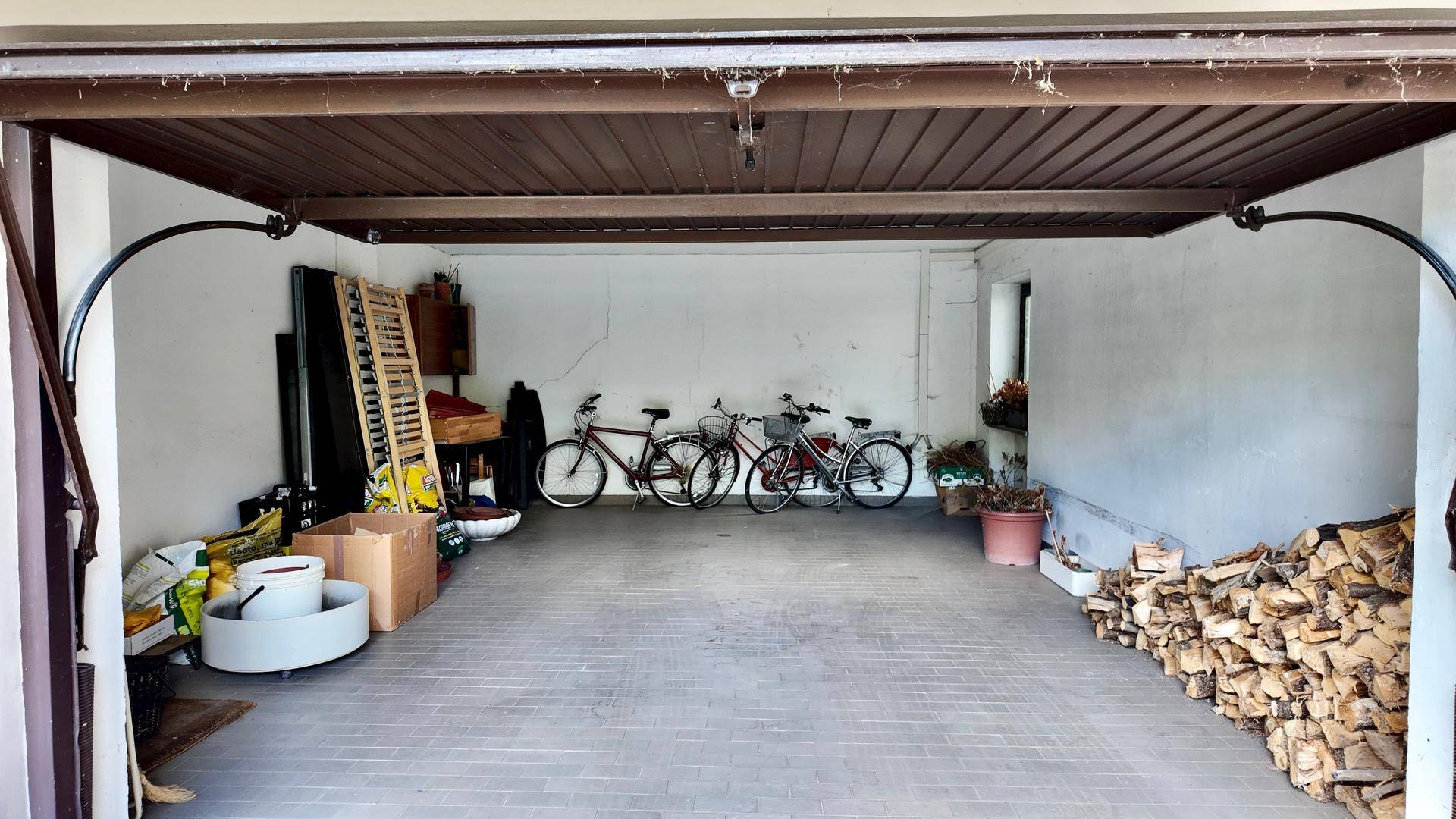 Geräumige Garage mit Platz für Fahrräder und Lagerung von Brennholz, mit Fliesenboden und weiß gestrichenen Wänden.