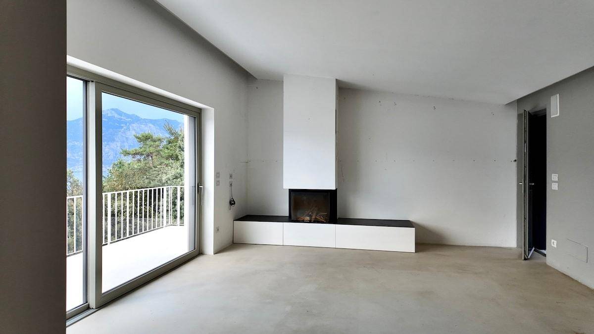Geräumiges Wohnzimmer mit Betonboden und modernem Kamin, bietet direkten Zugang zu einem Balkon mit Aussicht.