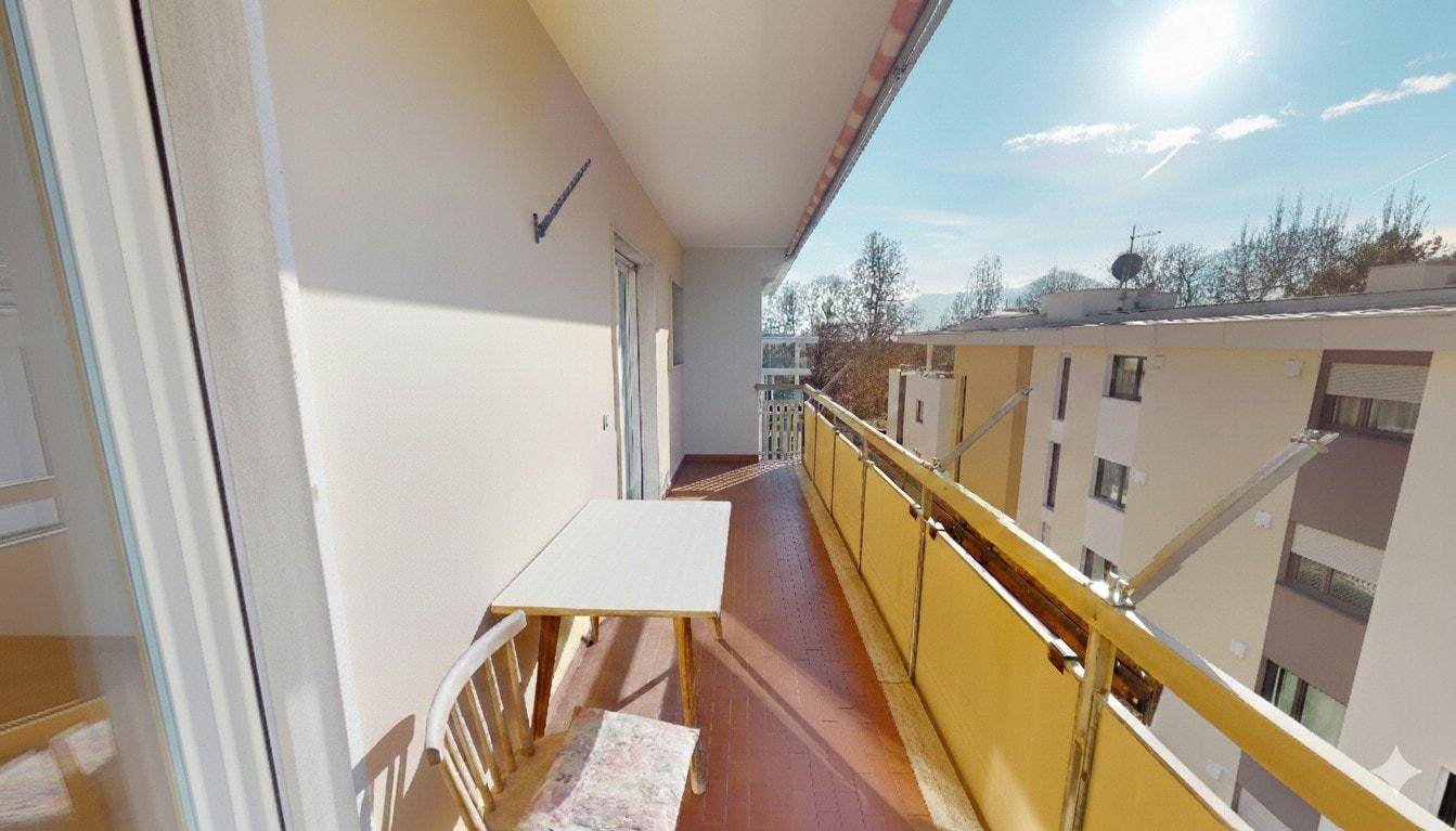Langer sonniger Balkon mit Sitzgelegenheiten und Blick auf die Umgebung.