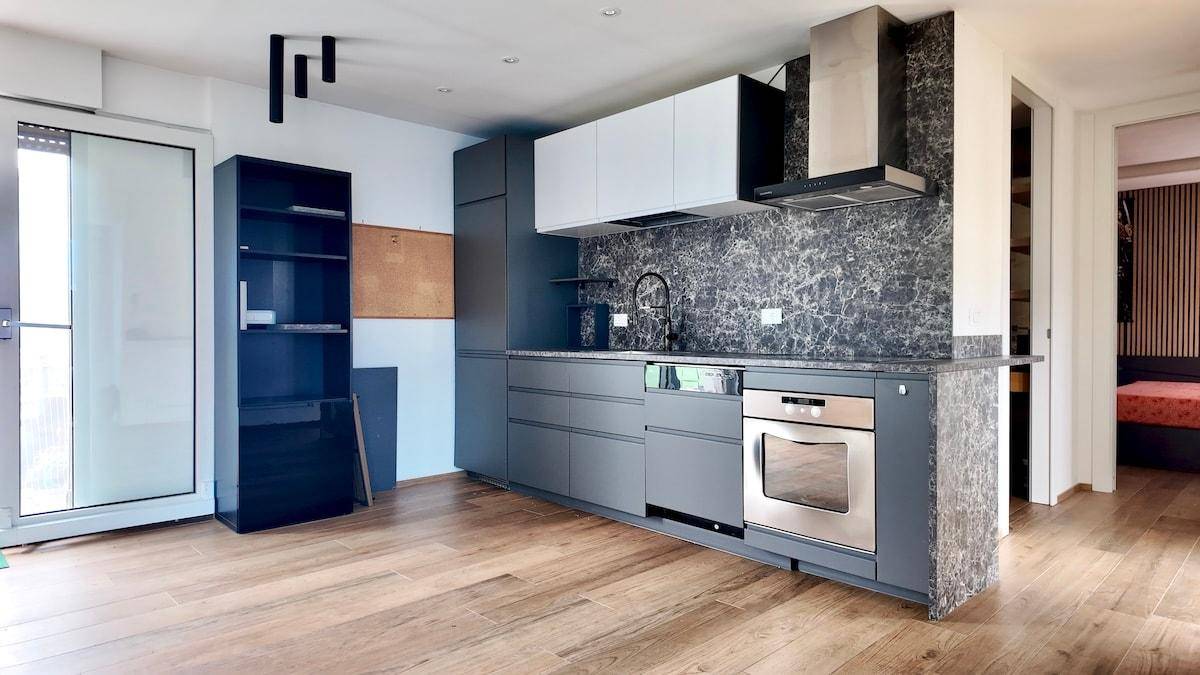 Moderne Küche mit grauen Schränken, integriertem Backofen und Holzboden.
