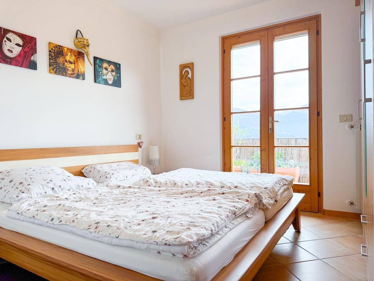 Schlafzimmer mit Doppelbett, Fliesenboden und direktem Zugang zu einem Balkon mit Bergblick.