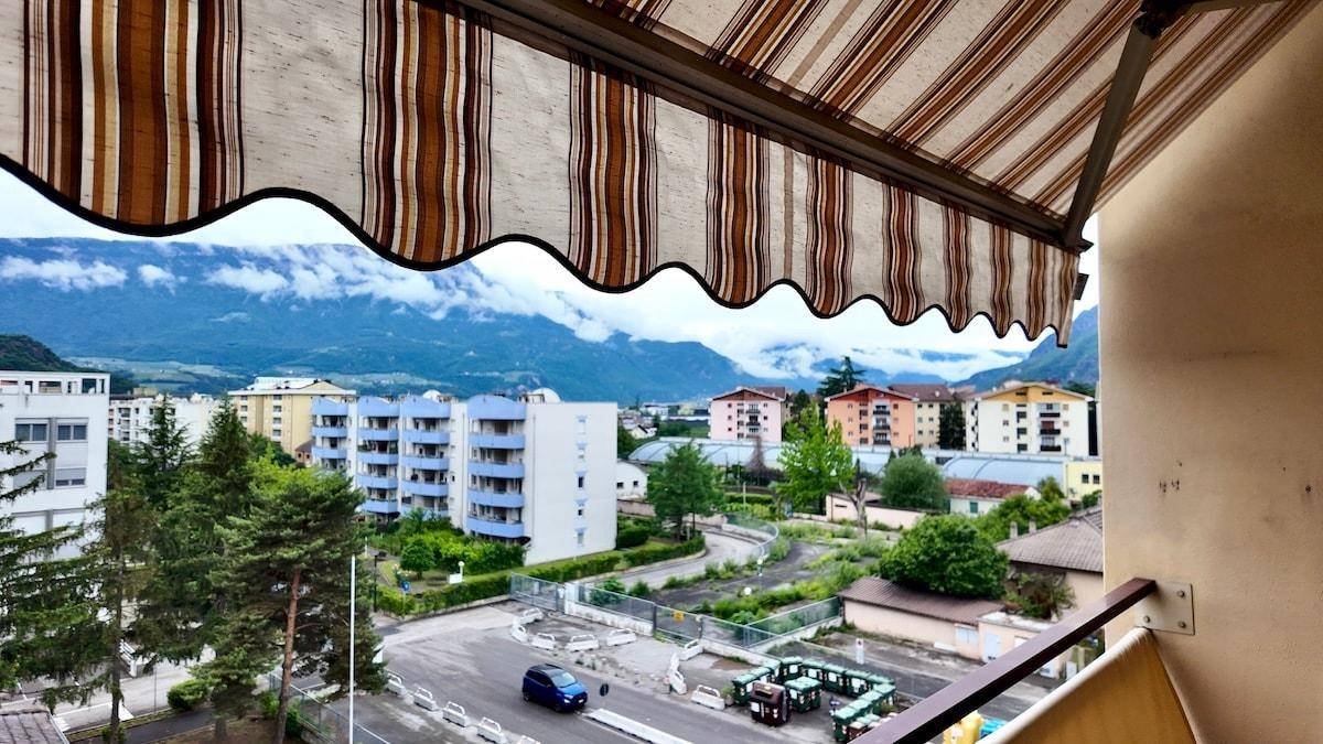 Balkon mit gestreifter Markise und Ausblick auf Wohngebiet und Berge.