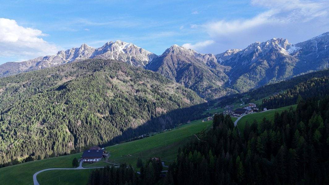 Malerische Bergkulisse mit schneebedeckten Gipfeln, dichten Wäldern und einem einzelnen Haus in der Ferne.
