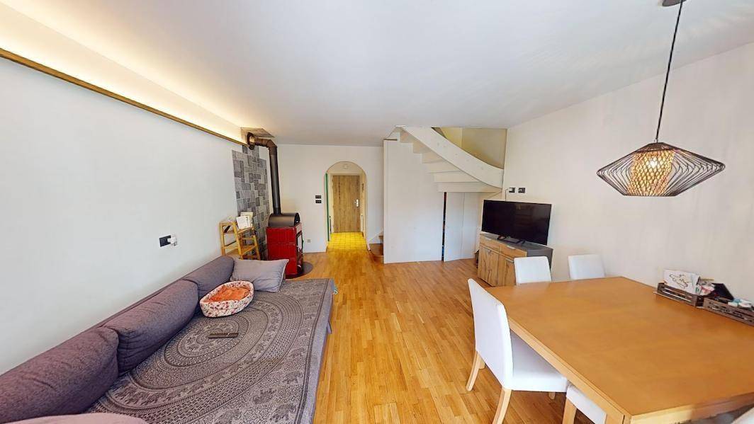 Offener Wohn-Essbereich mit Holzboden, Kaminofen und Treppe zum Obergeschoss.