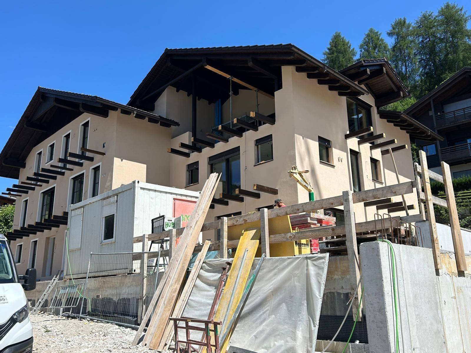 Seitenansicht des Neubaus mit beiger Fassade und dunklem Dach, umgeben von Baumaterialien.